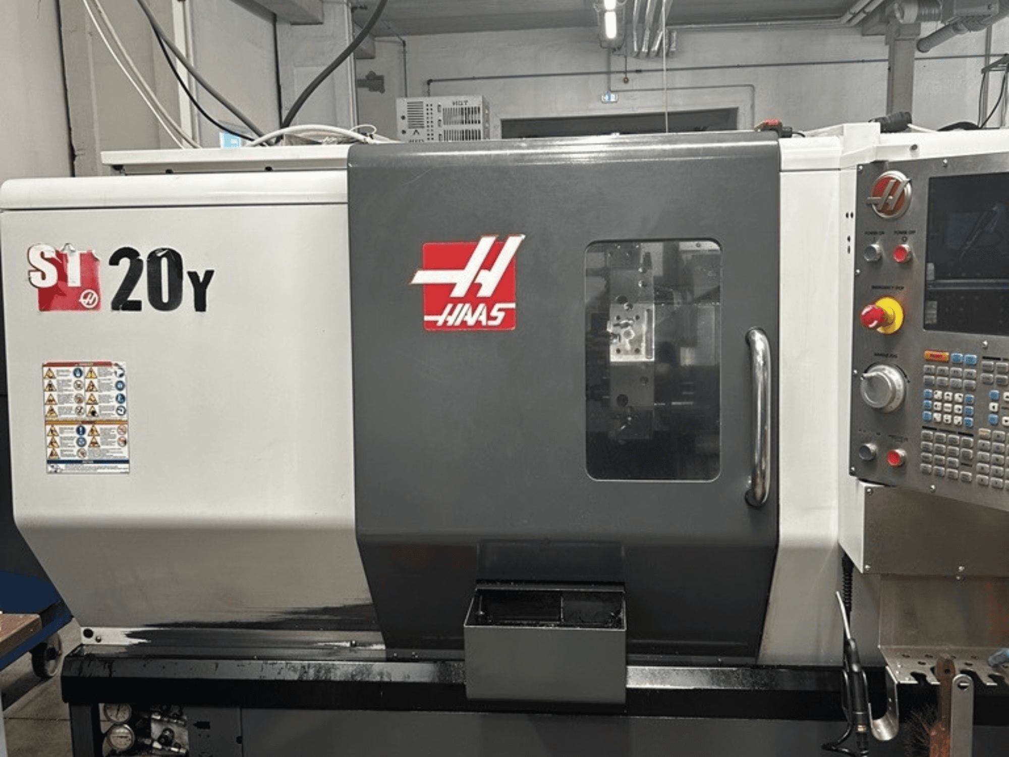 Torno CNC Haas ST-20Y, vista frontal, mostrando o painel de controlo, etiquetas de segurança e janela operacional.
