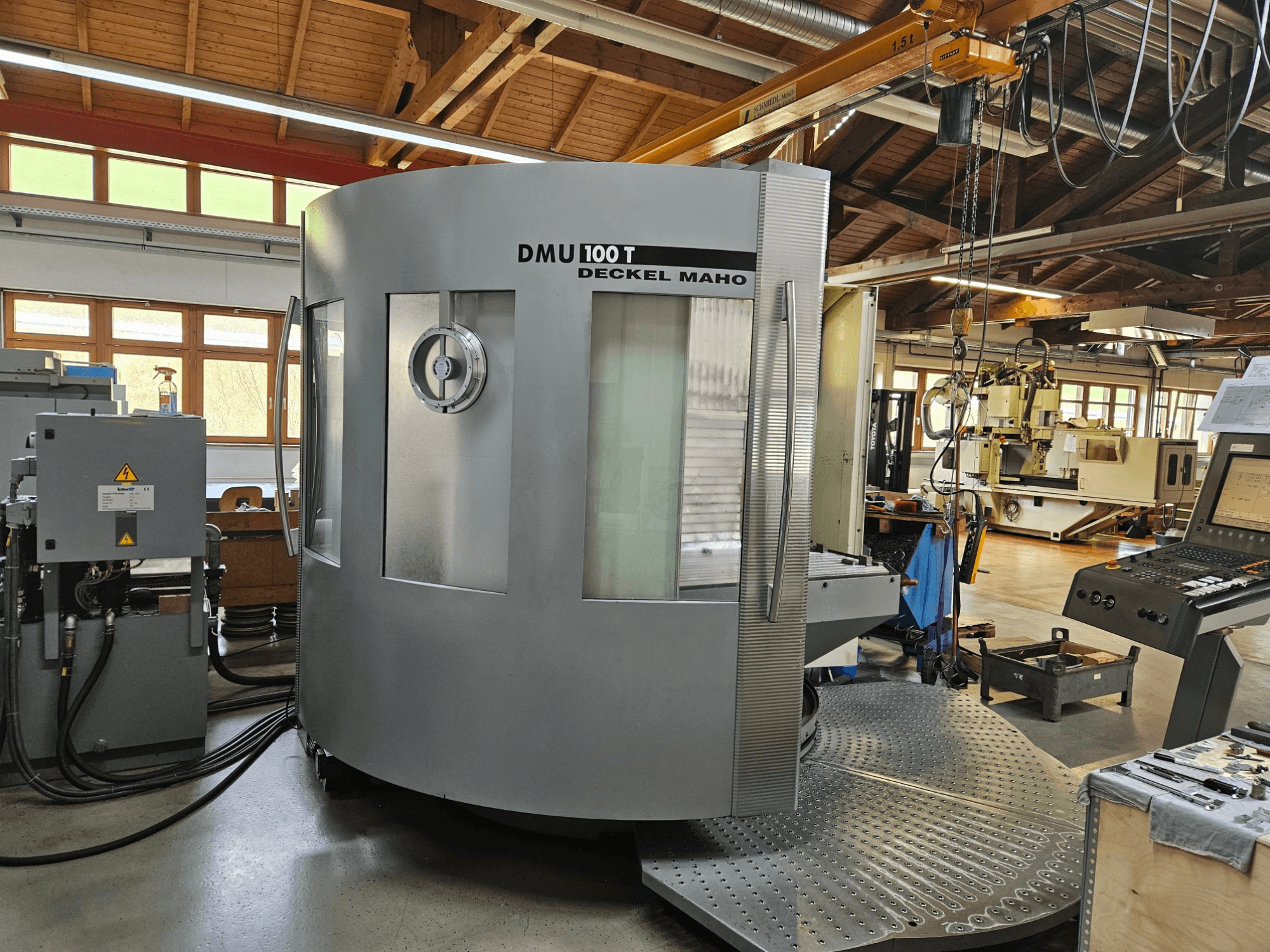 Máquina CNC DMU 100 T Deckel Maho vista de frente, com uma grande base circular, painel de controlo e caixa de vidro.
