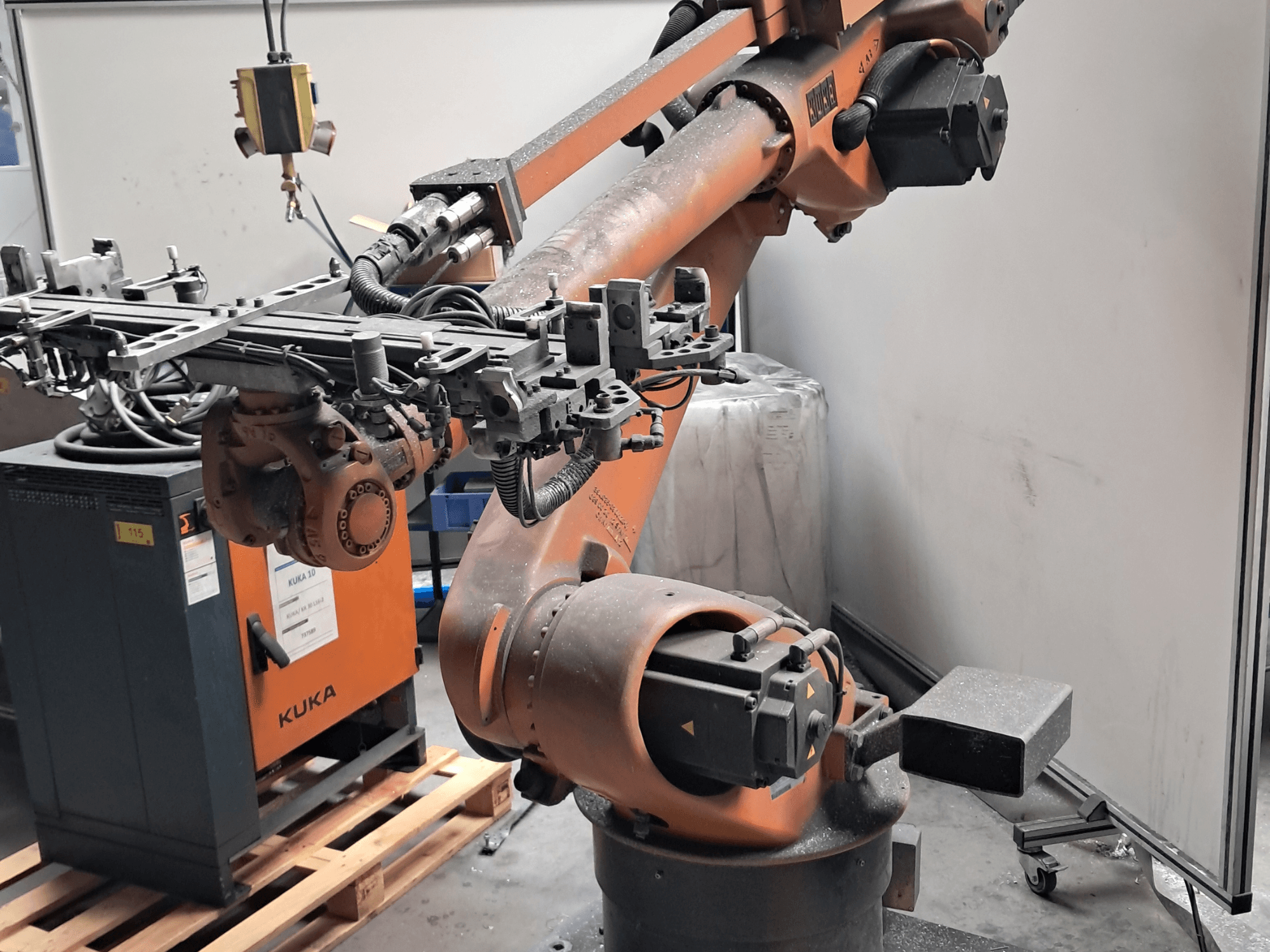 Braço robótico KUKA KR 30L16-2 visto de perfil, com um efetor final complexo e cabos de controlo, colocado ao lado de uma caixa de controlo KUKA.