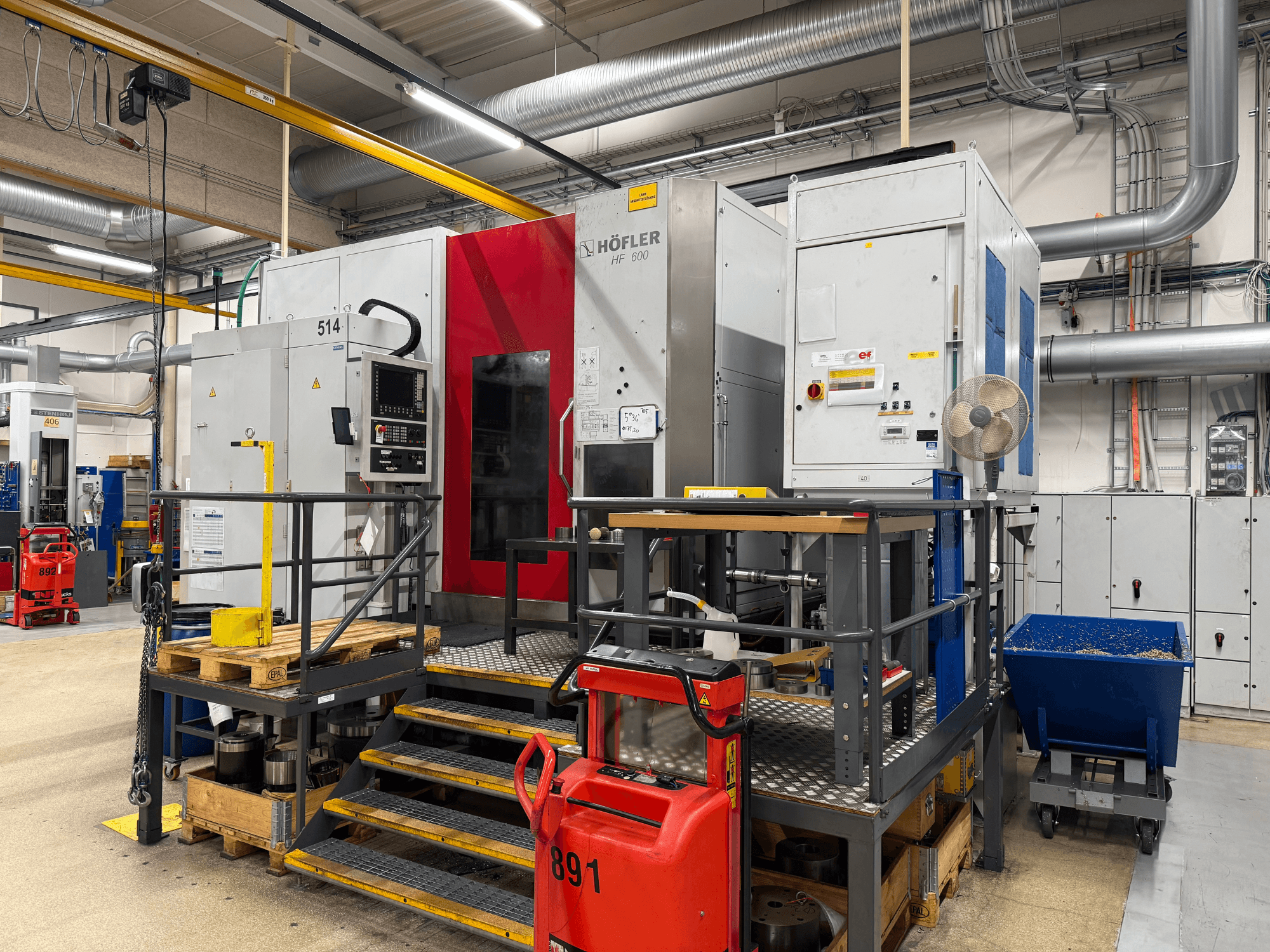 Máquina-ferramenta HOFLER HF 600, vista lateral, mostrando o painel de controlo, a barreira de segurança amarela e o ambiente circundante da oficina.