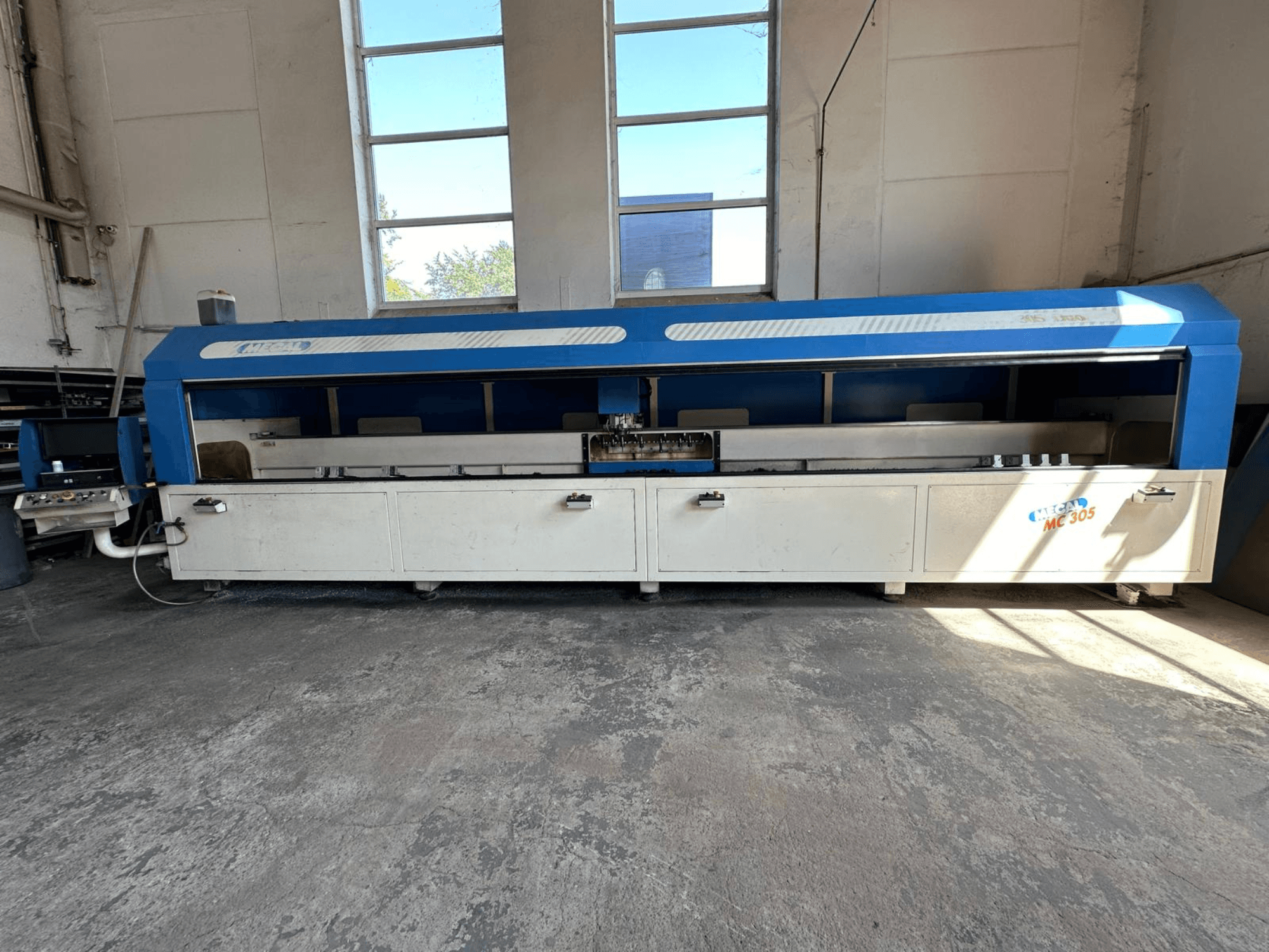 Vista frontal do centro de maquinação vertical MECAL MC 305, com um design azul e branco, mesa de trabalho visível e painel de controlo.