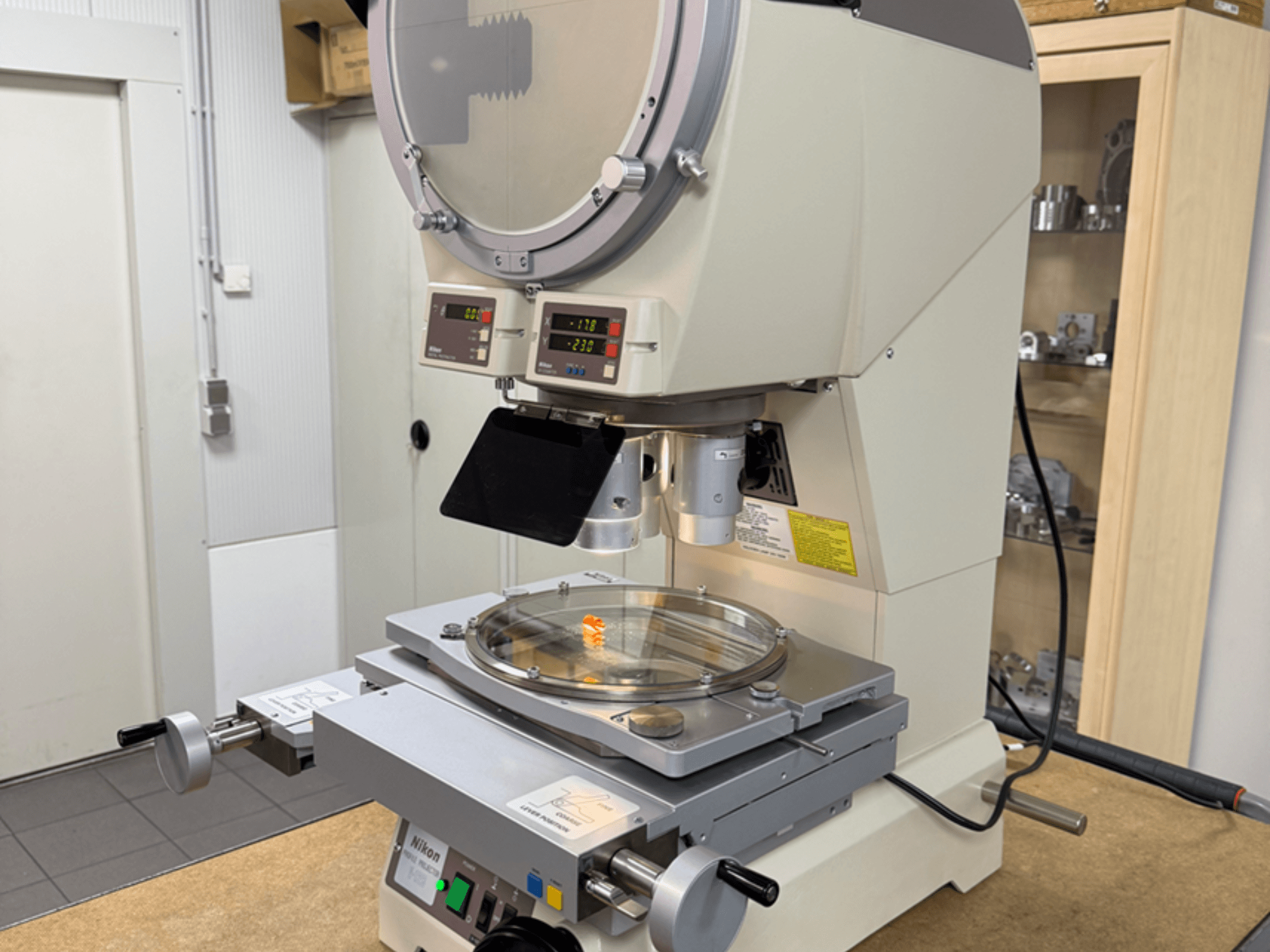 Microscópio modelo Nikon numa vista frontal, com ecrãs digitais, uma plataforma ajustável e uma placa de vidro circular.