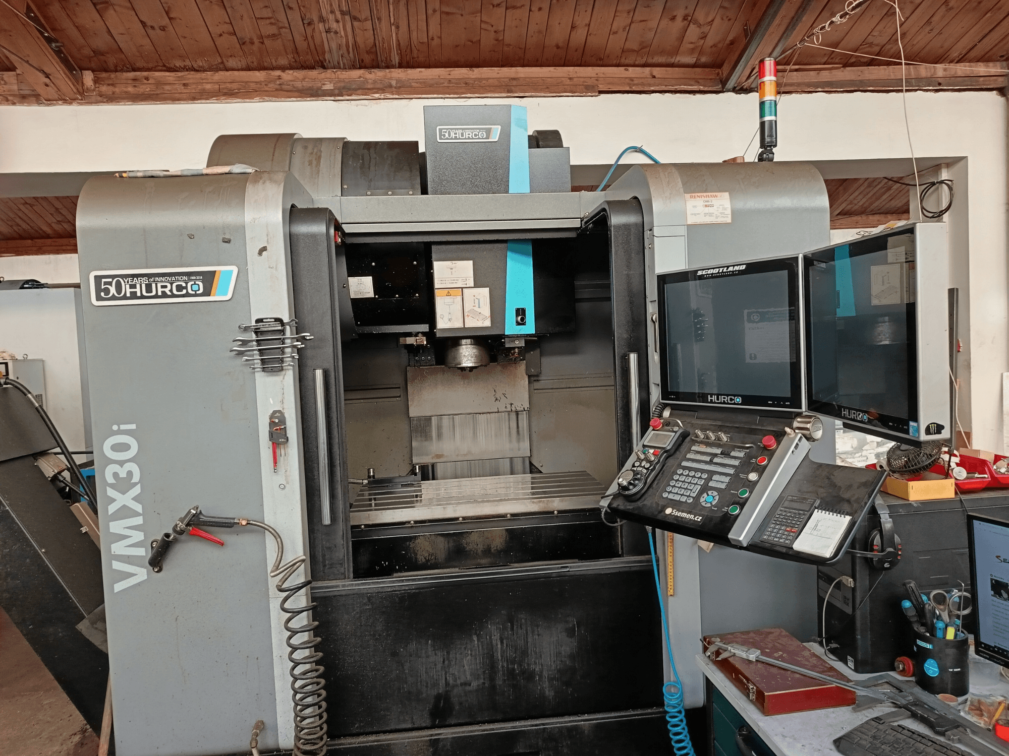 Fresadora CNC Hurco VMX30i em vista frontal, com dois monitores, painel de controlo e uma mangueira ligada.