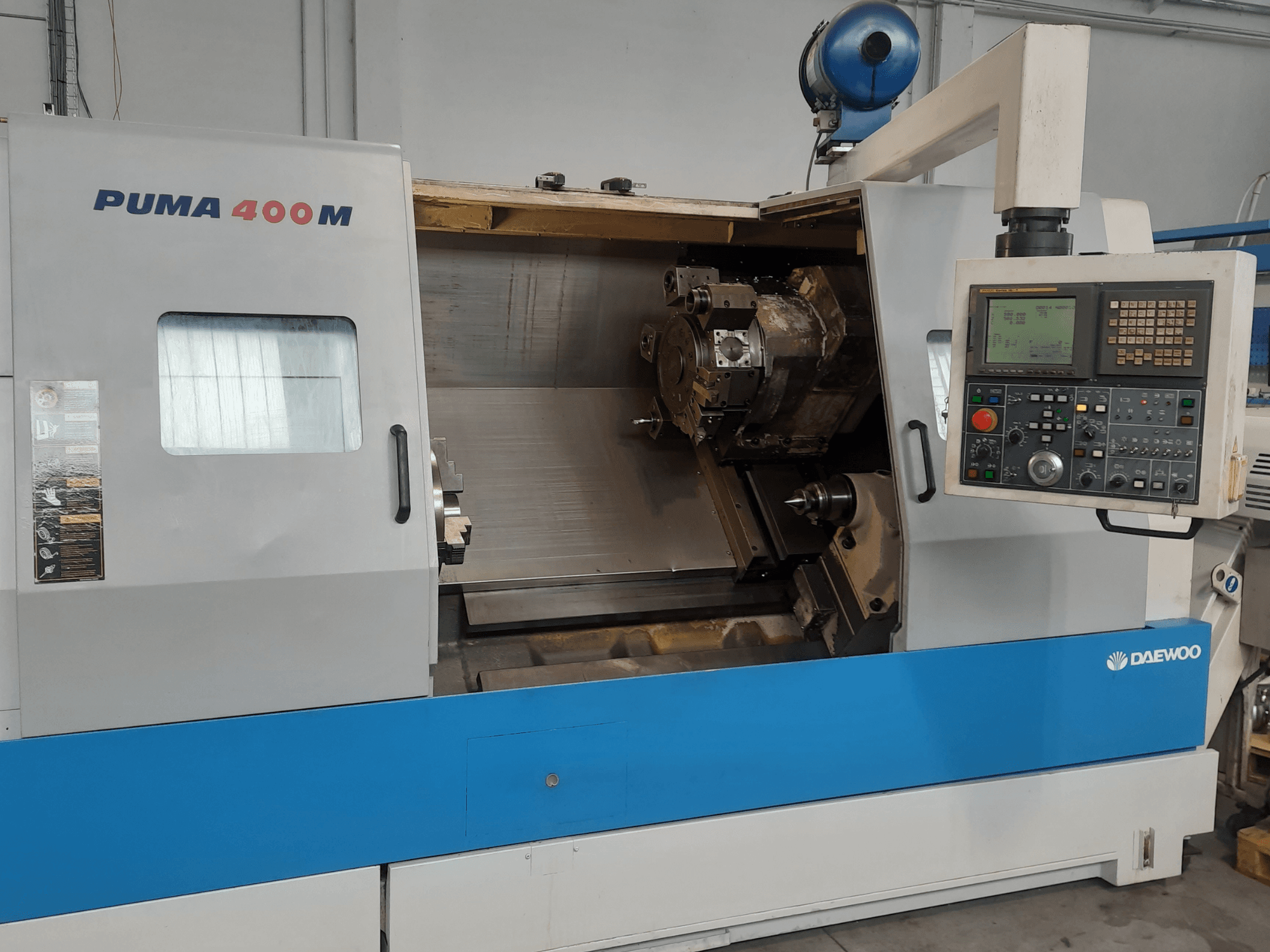 Vista frontal de uma máquina de torneamento horizontal DAEWOO PUMA 400MB, mostrando os comandos e a ferramenta de corte na câmara.