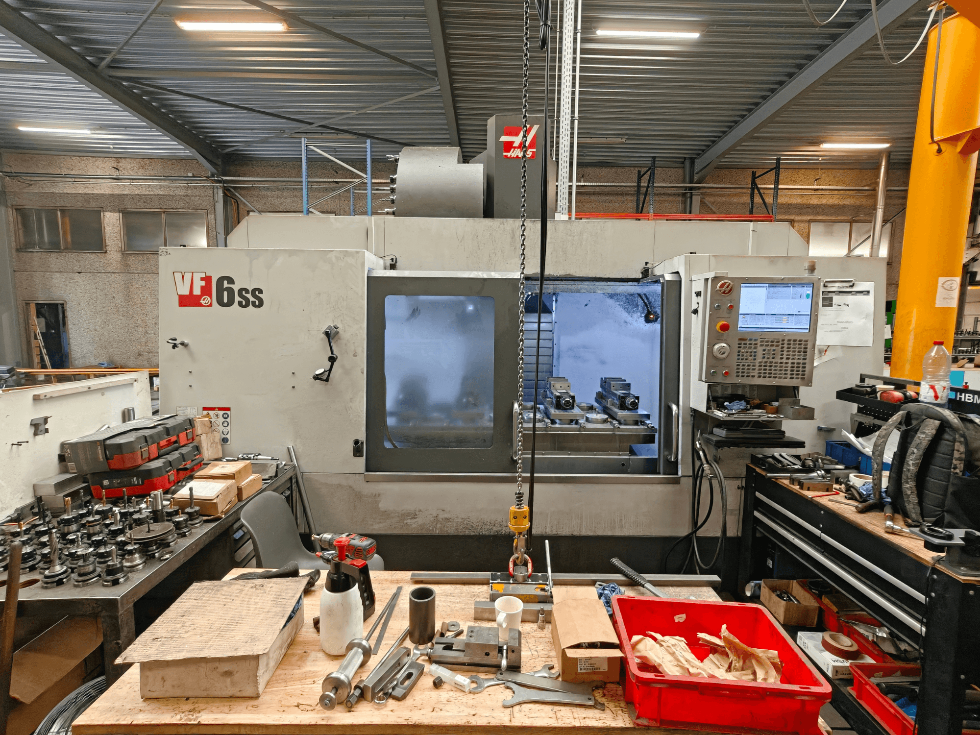 Centro de maquinagem vertical Haas VF-6SS numa oficina, vista lateral que mostra o painel de controlo e a área de trabalho repleta de ferramentas.