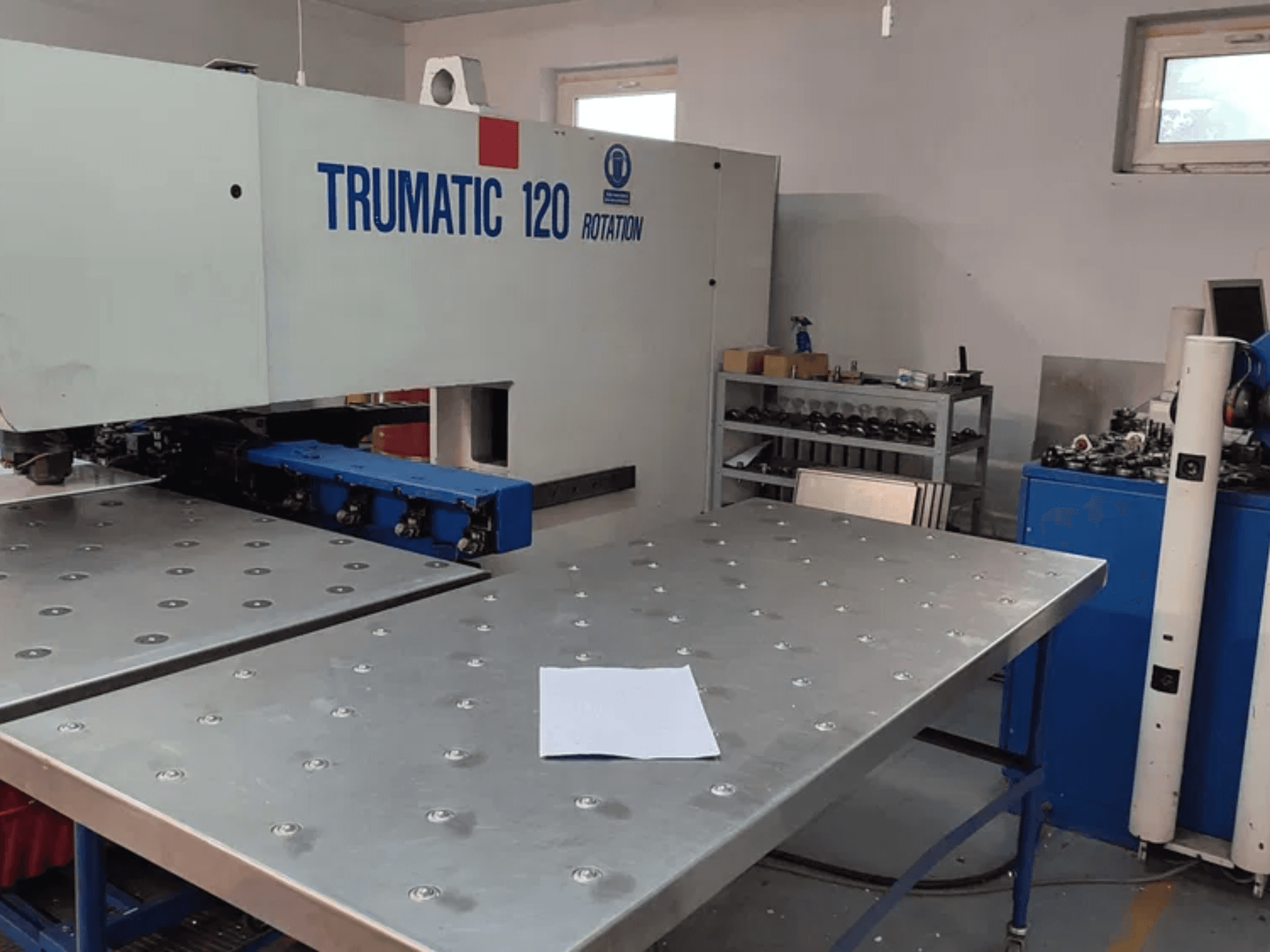 Puncionadora TRUMPF TRUMATIC 120R CNC vista de frente, com uma mesa metálica com furos e uma folha em branco.