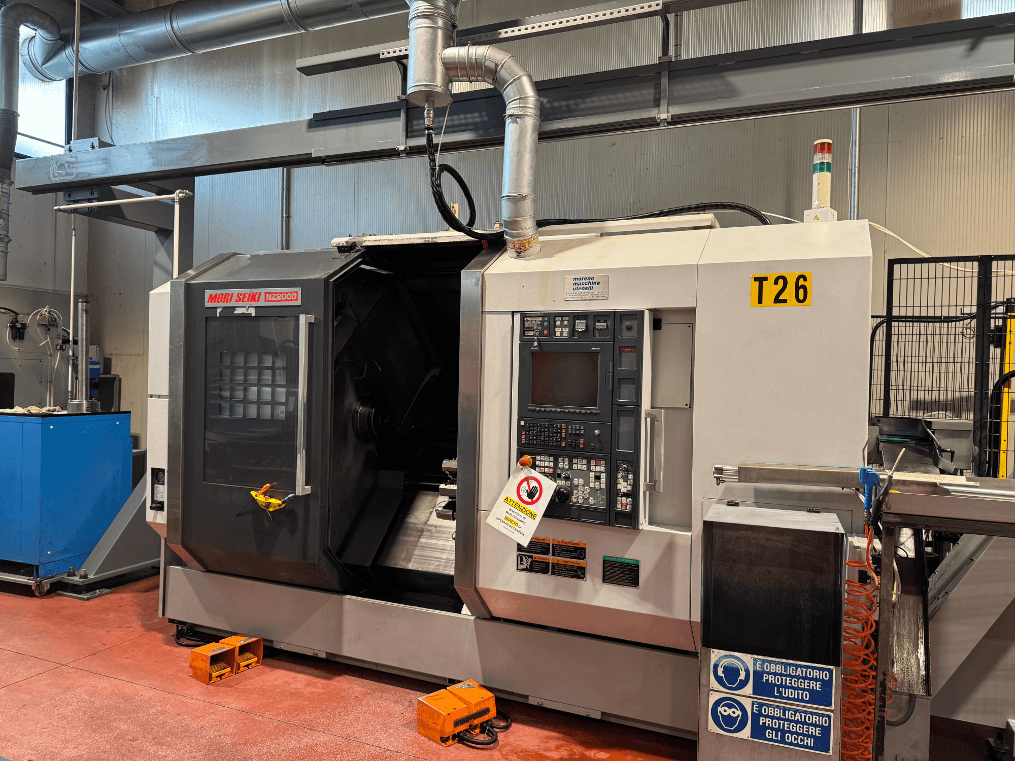 Centro de torneamento MORI SEIKI NZ-2000/T2/Y2, vista frontal, com painel de controlo, sinalização de segurança e configuração industrial.