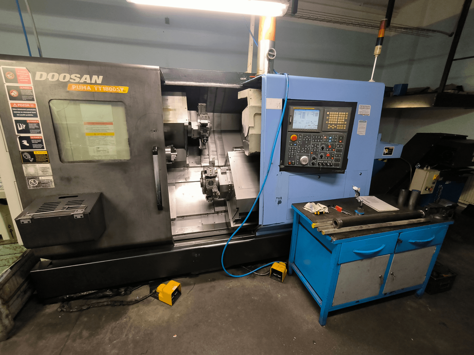 Torno CNC Doosan Puma TT1800SY, vista frontal, mostrando o painel de controlo, área de trabalho com ferramentas e componentes da máquina.