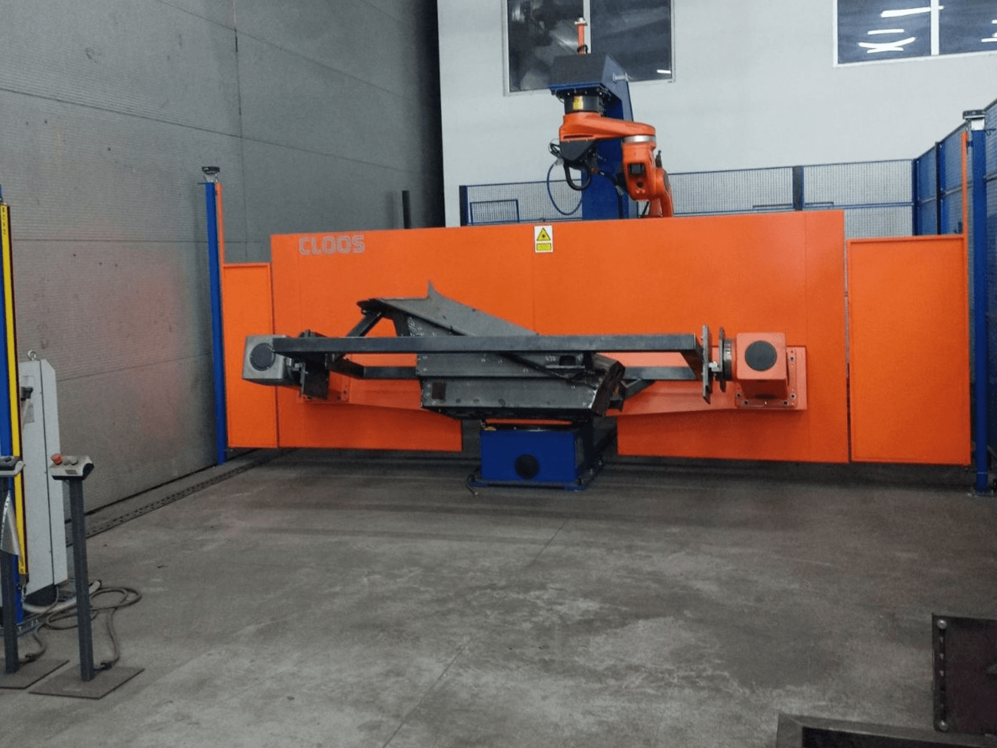 Vista frontal do sistema de automação CLOOS QIROX QRC-350-E com braço robótico e estrutura metálica em ambiente industrial.