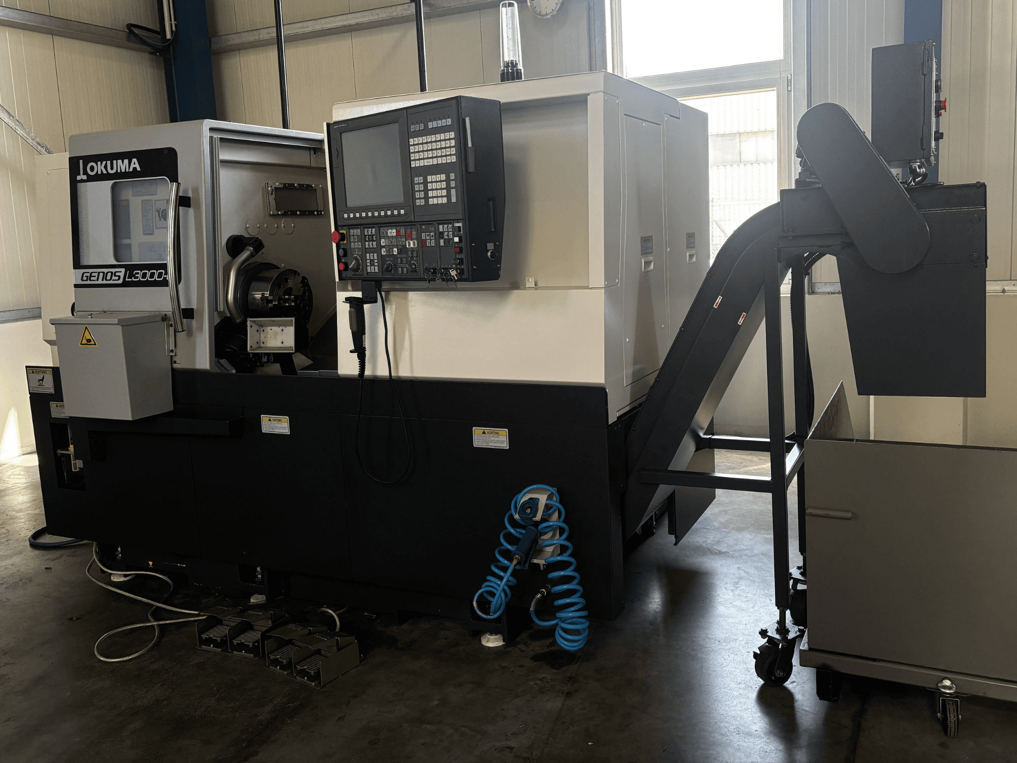 Torno horizontal Okuma GENOS L3000-e, vista frontal, com painel de controlo, transportador e área do fuso visível.