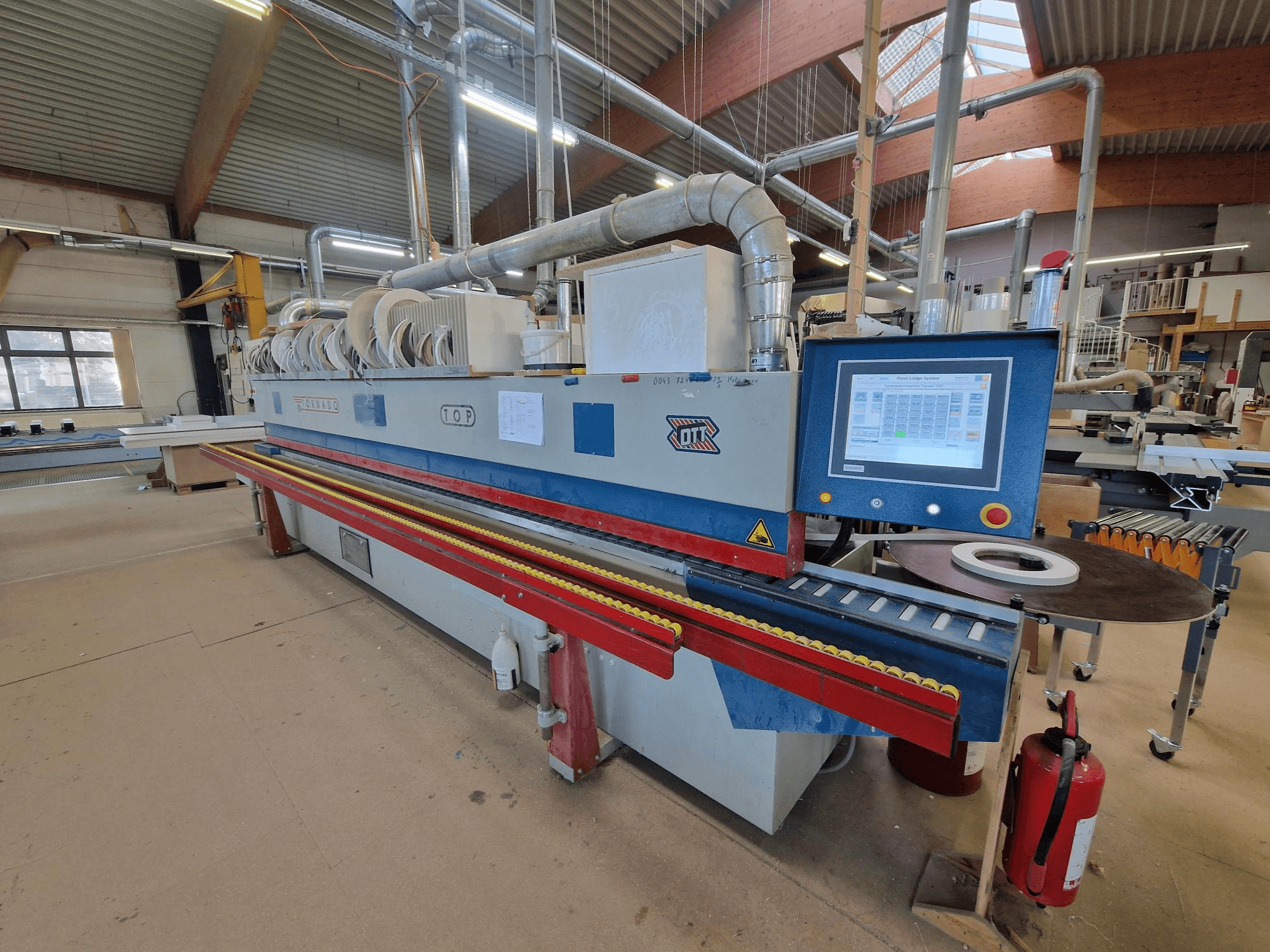 Máquina de colar bordas OTT Tornado, vista frontal, mostrando o painel de controlo, os rolos de alimentação e a área de aplicação do adesivo.