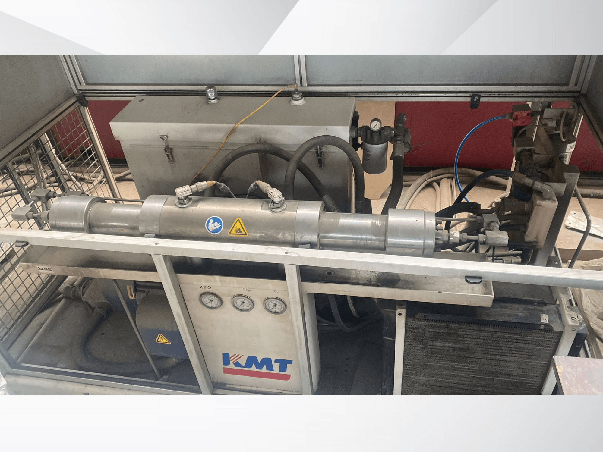 Máquina hidráulica KMT em vista frontal, com manómetros, mangueiras e uma caixa metálica, ideal para aplicações industriais.