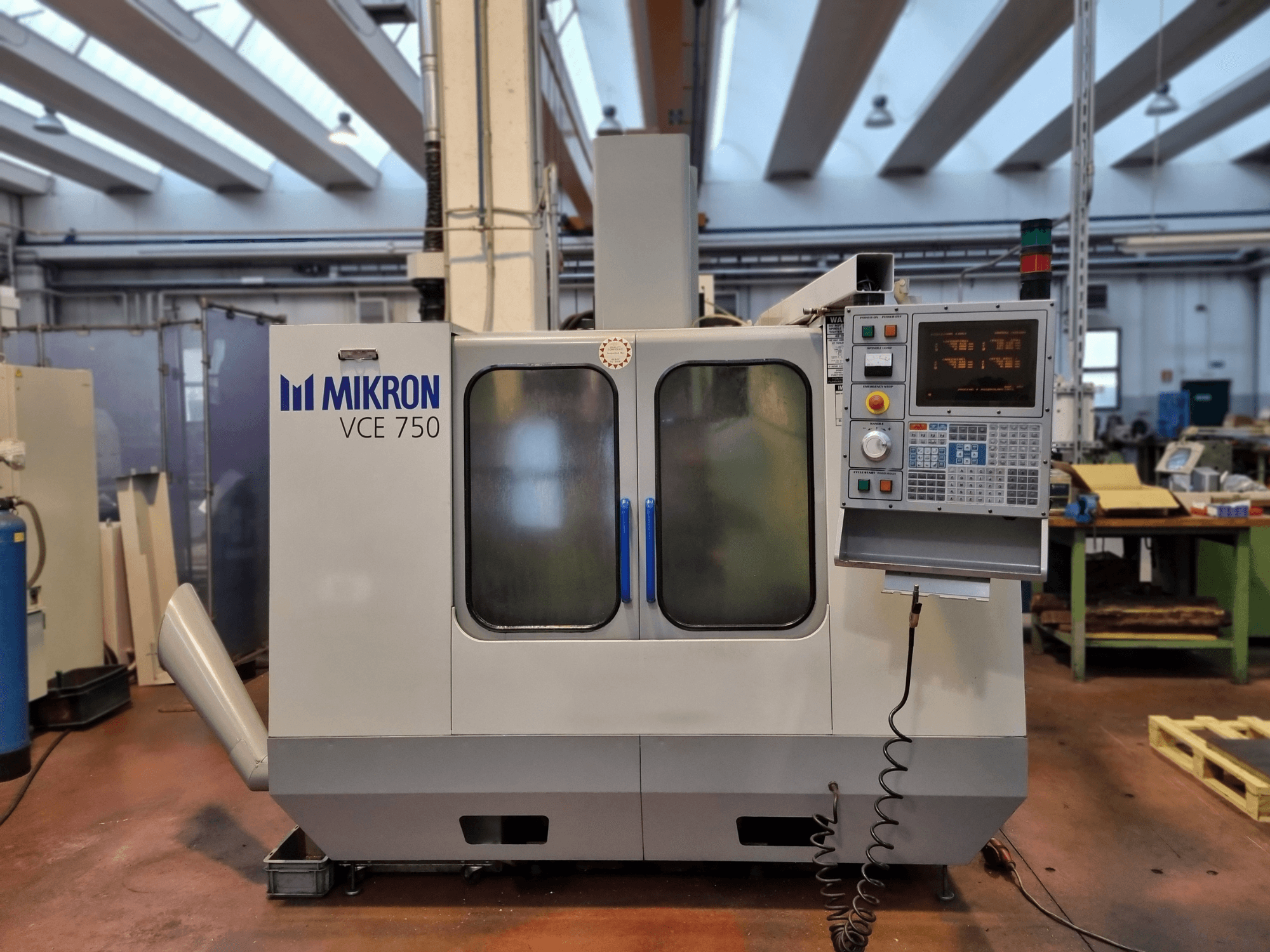 Máquina CNC Mikron VCE 750 branca numa oficina, vista lateral, com um painel de controlo digital e grandes portas de vidro.