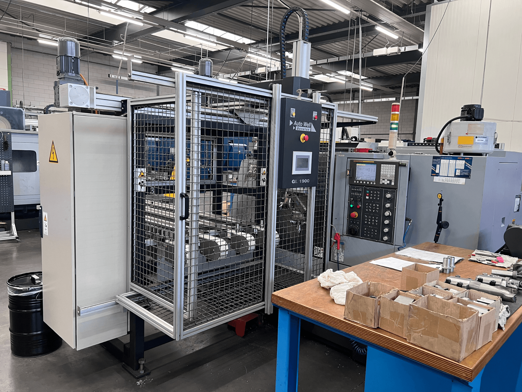 Vista frontal da máquina Auto Weld GL 1900 com painel de controlo, caixa de segurança e ferramentas circundantes numa bancada de trabalho.