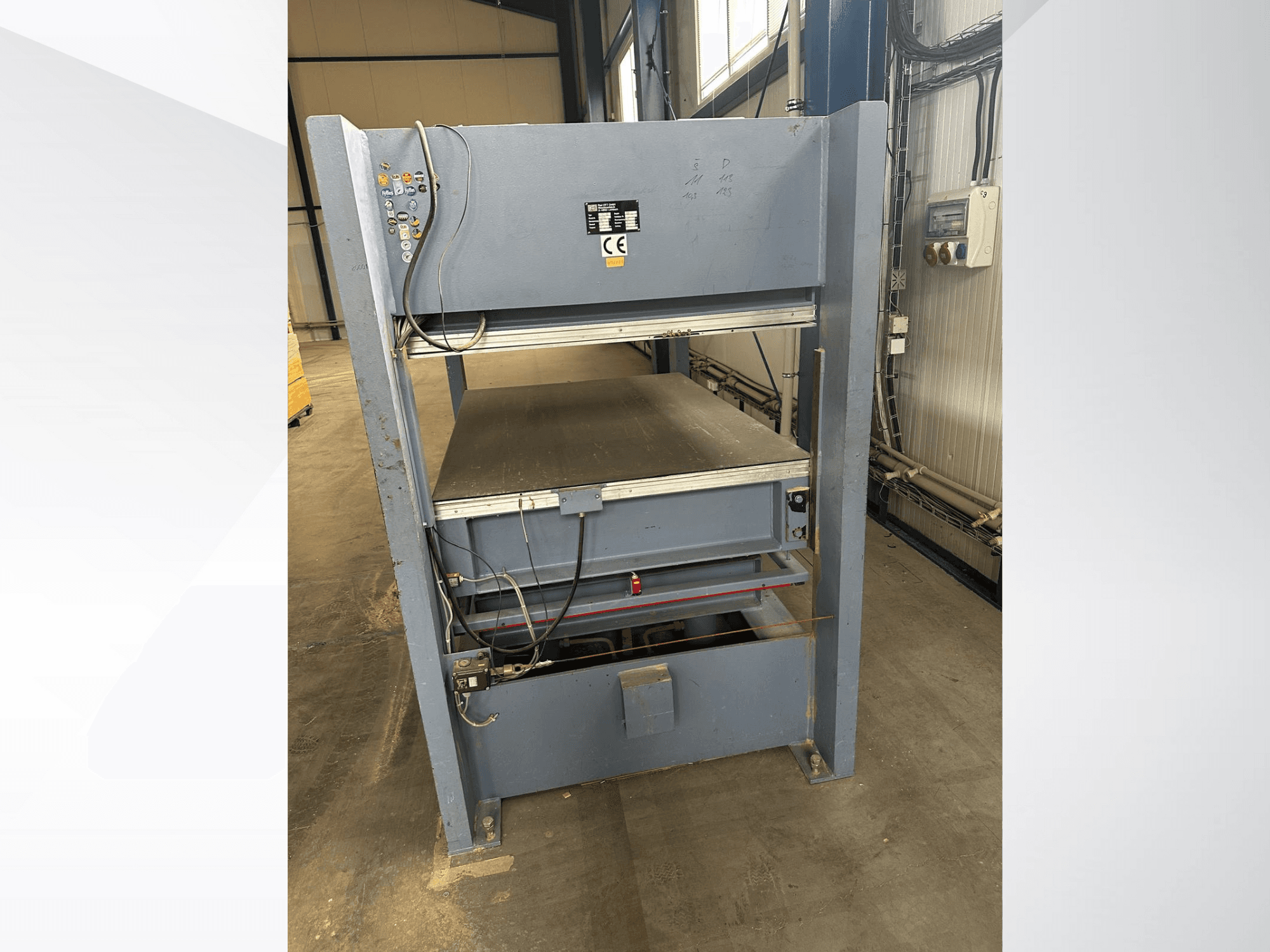 Máquina industrial cinzenta com painel de controlo, vista de frente; inclui plataformas ajustáveis e marcações de segurança.