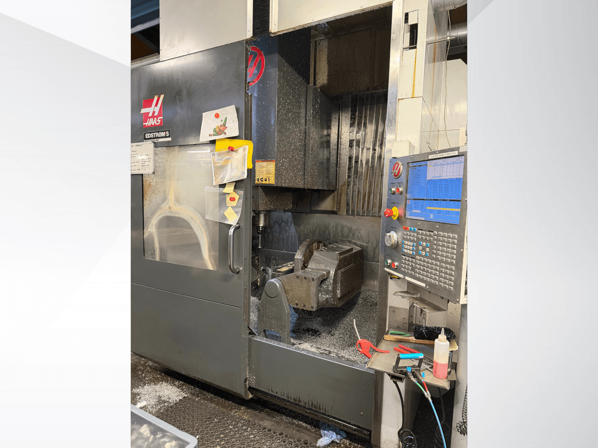 Máquina CNC Haas modelo EDSTROM S, vista frontal, com peça de trabalho em metal, painel de controlo e aparas de metal no interior.