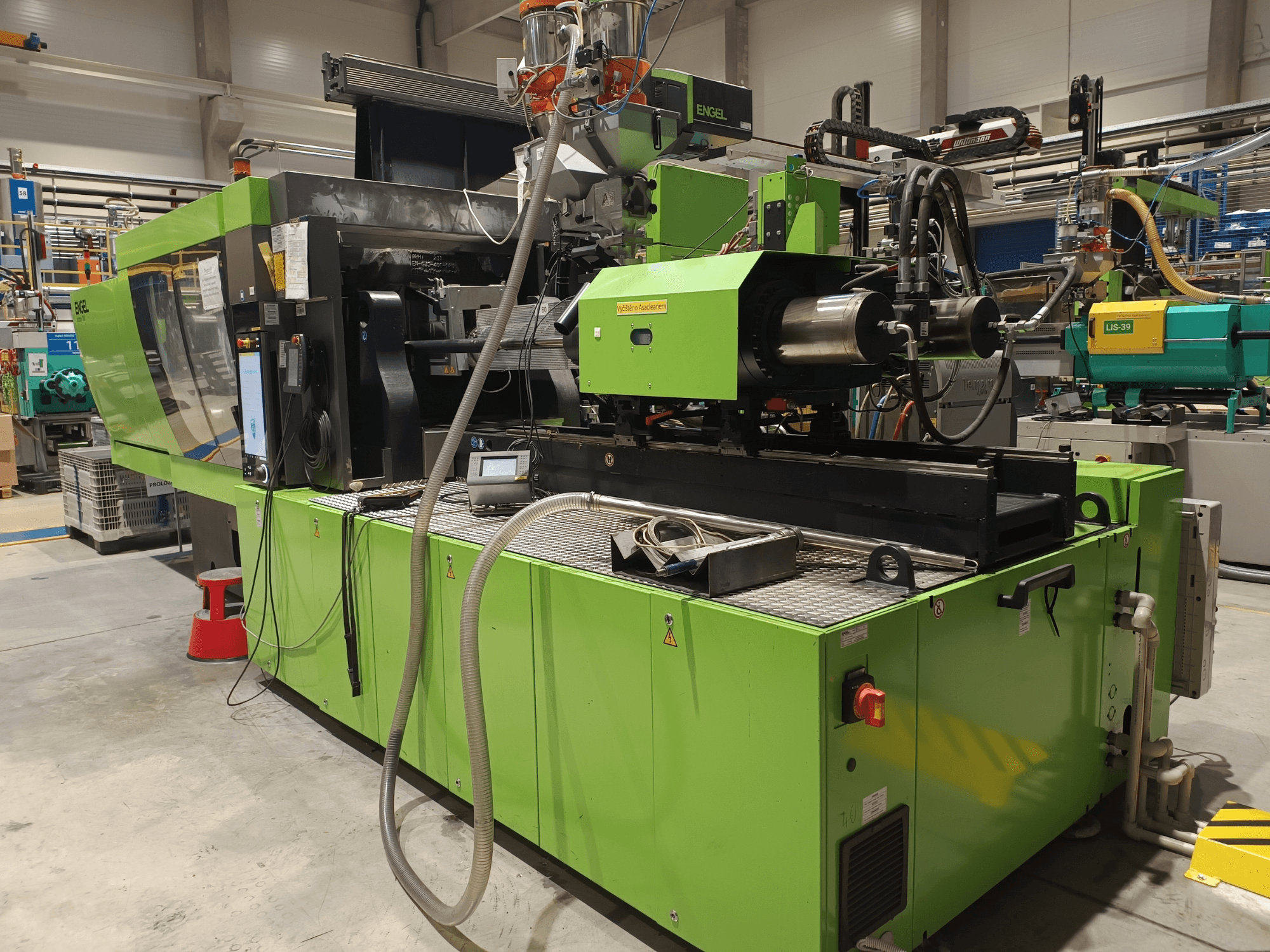 Máquina de moldagem por injeção Engel, vista lateral, exterior verde, com painel de ecrã tátil e componentes hidráulicos visíveis.