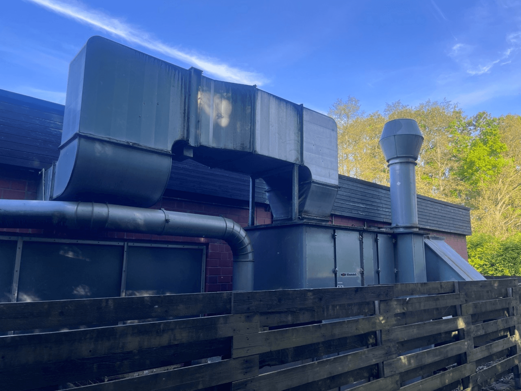 Sistema de ventilação industrial com condutas metálicas, vista lateral; inclui uma chaminé quadrada e cilíndrica, acabamento verde.