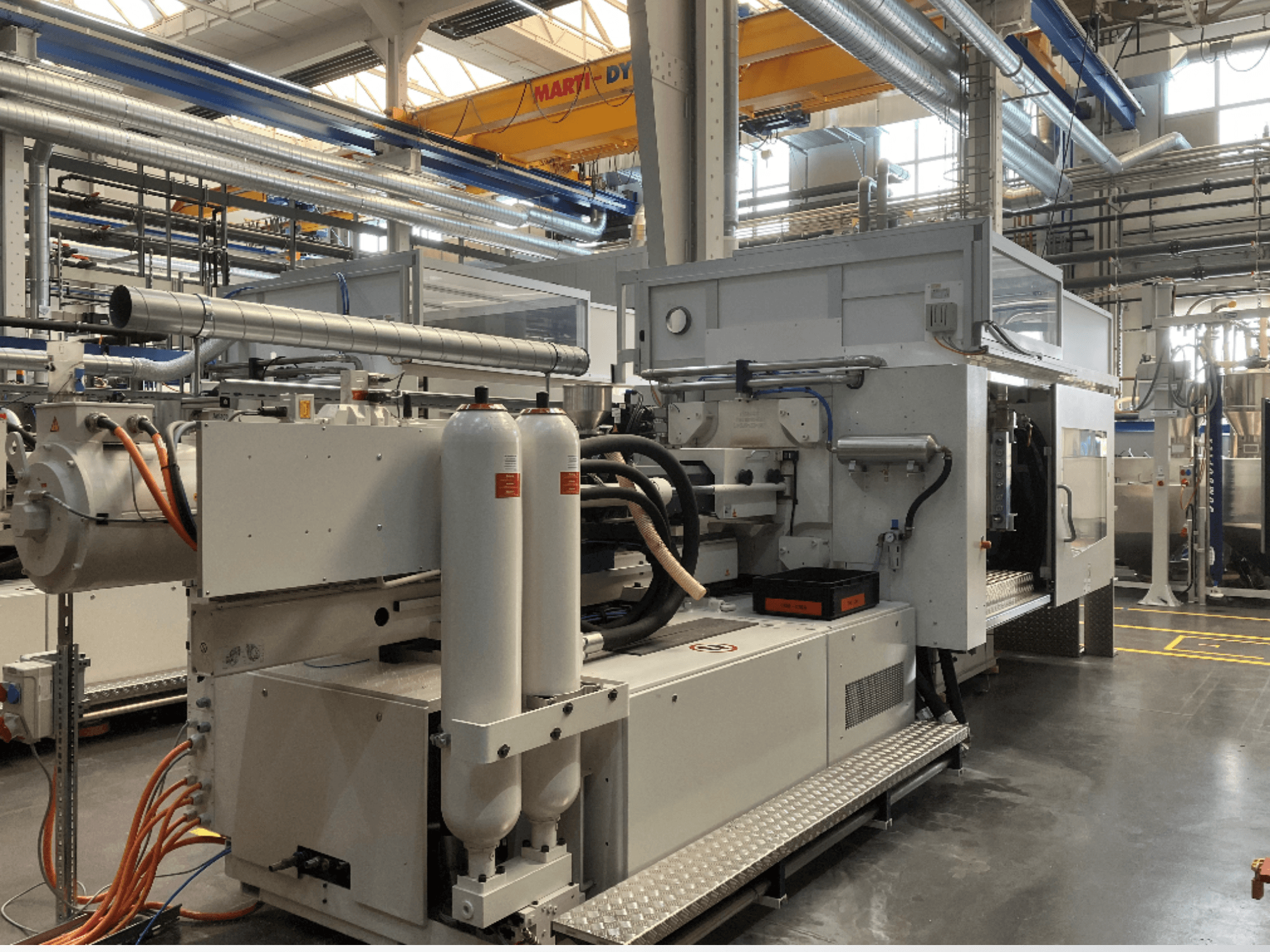 Máquina industrial mostrada em vista lateral com várias mangueiras, dois tanques verticais e painel de controlo; marca/modelo não visível.