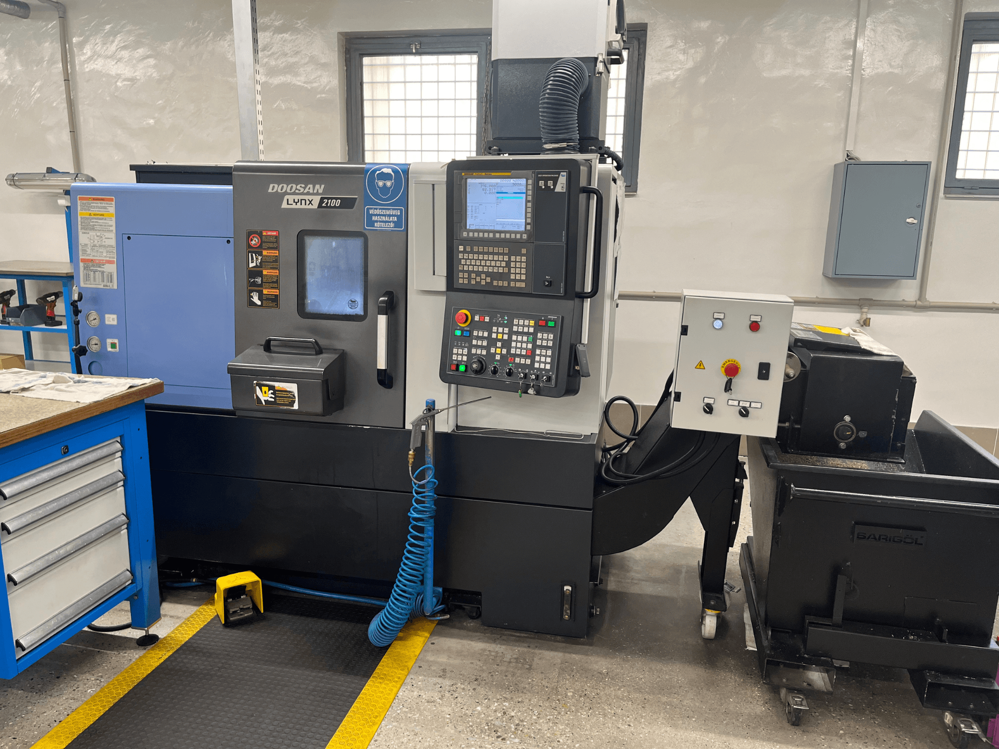 Torno Doosan Lynx 210 na oficina, mostrando o painel de controlo, o armazenamento de ferramentas e o sistema de refrigeração, vista lateral com detalhes do espaço de trabalho.