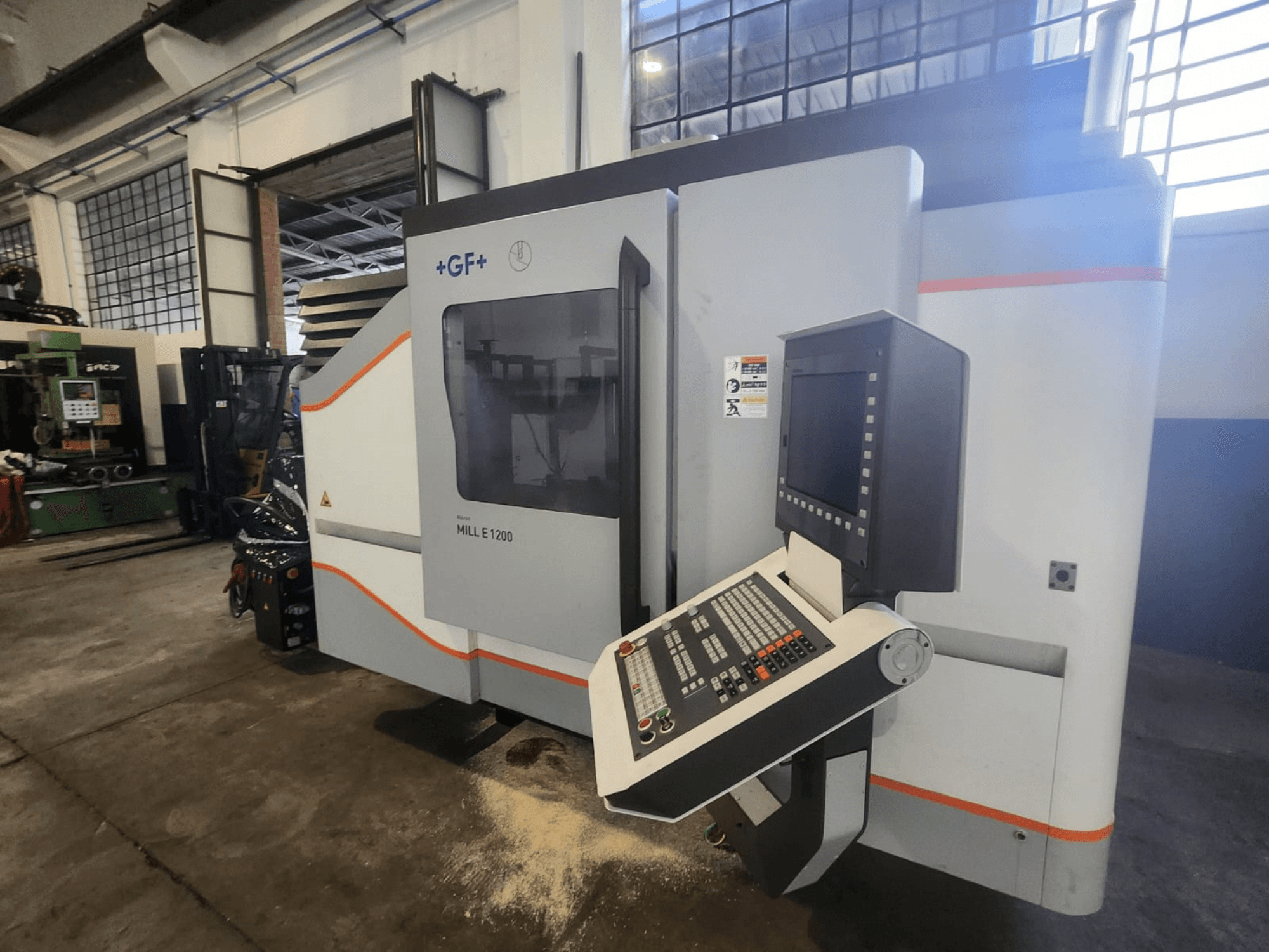 GF MILL E1200, vista frontal da fresadora com painel de controlo, ecrã de visualização e etiquetas de segurança, em ambiente de oficina.