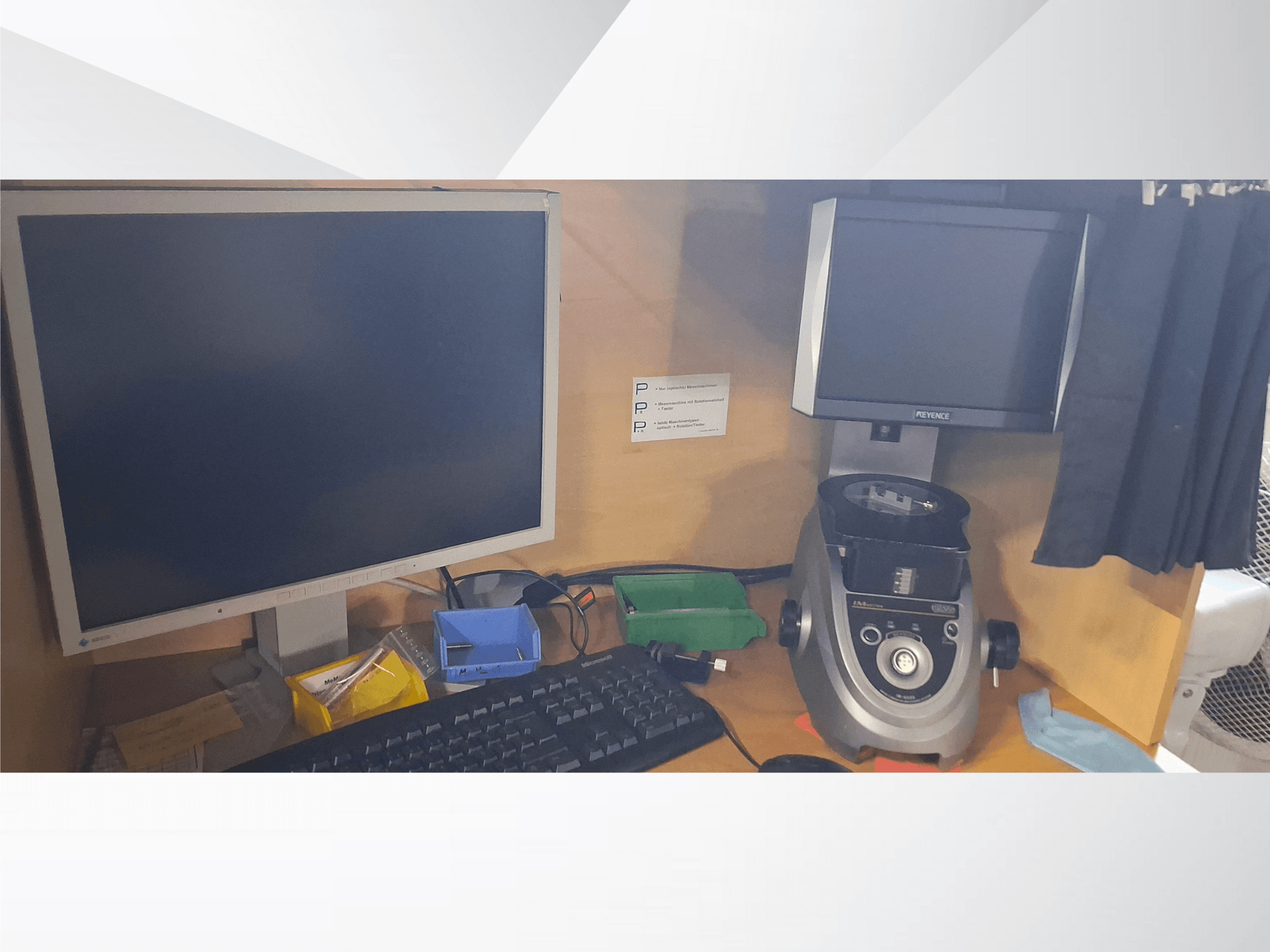 Monitor de computador com teclado, ecrã da marca PEVA e um dispositivo de laboratório cinzento numa secretária de madeira com vários tabuleiros e papelada.