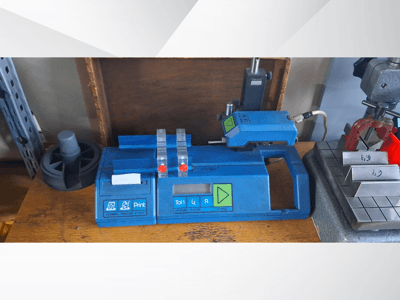 Impressora Hommel T 1000 azul e aparelho de teste T 1 010 com botões vermelhos, vistos de frente numa bancada com blocos metálicos.