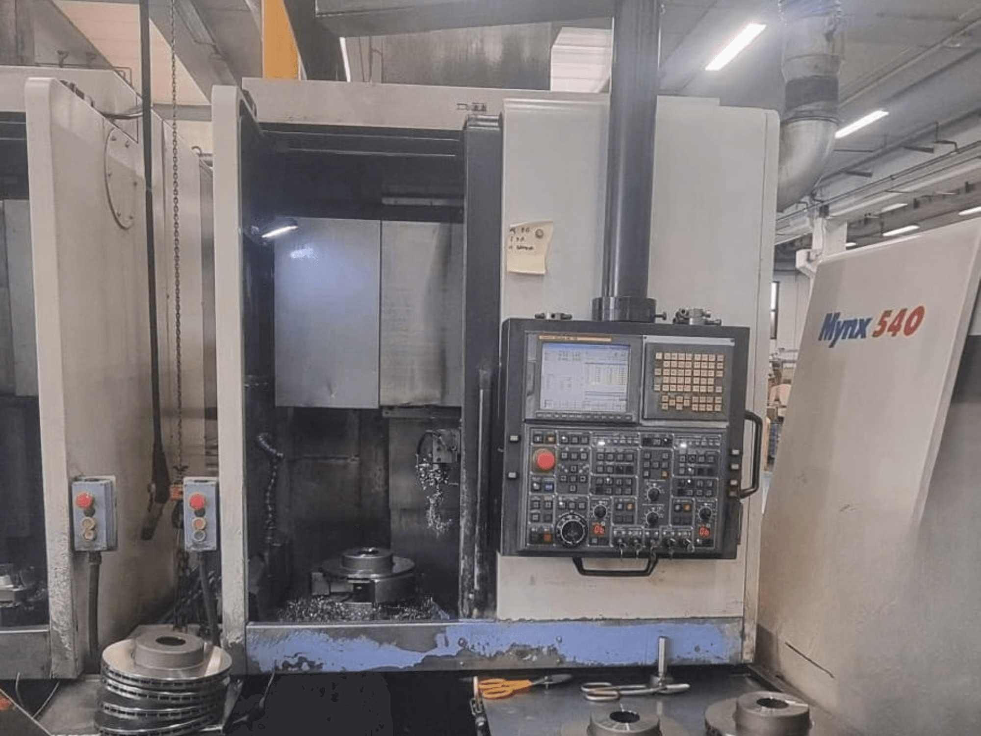 Vista frontal de um torno vertical DOOSAN PUMA V400-2SP, mostrando o painel de controlo e a configuração da peça de trabalho no interior da máquina.
