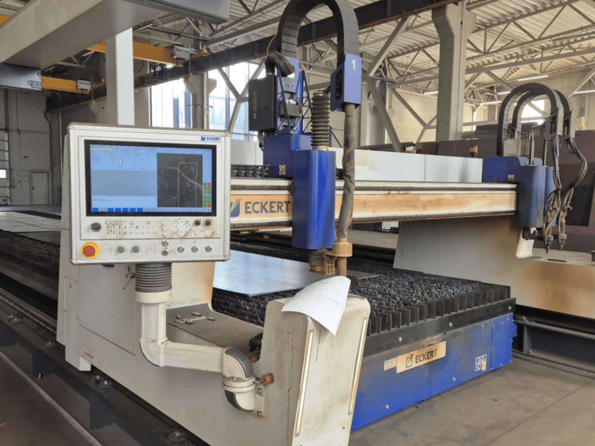 Painel de controlo da máquina de corte CNC ECKERT em vista frontal, com um ecrã tátil e vários botões operacionais.