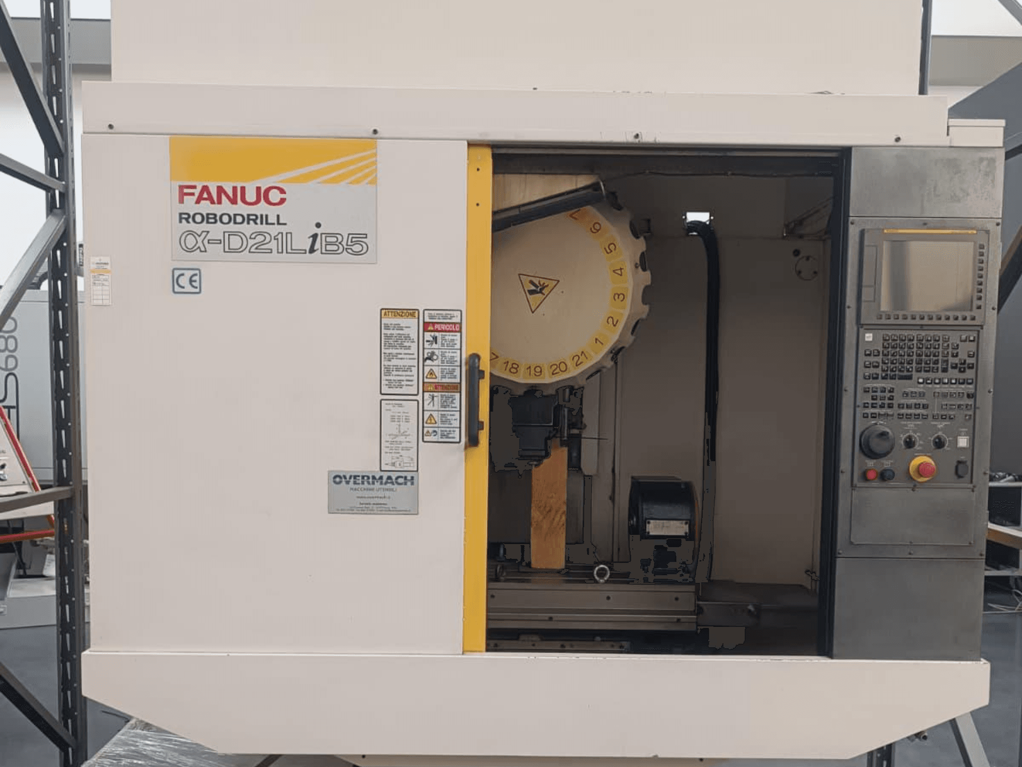FANUC Robodrill α-D21LiB5, vista frontal; máquina CNC com suporte de ferramentas, painel de controlo e avisos de segurança visíveis.