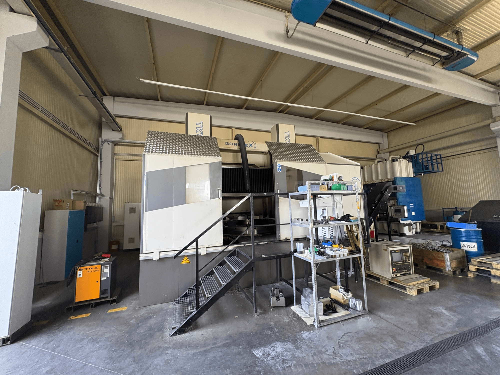 Configuração de maquinação industrial com máquina GORAT X, vista lateral; inclui ferramentas, painel de controlo e equipamento em prateleiras.