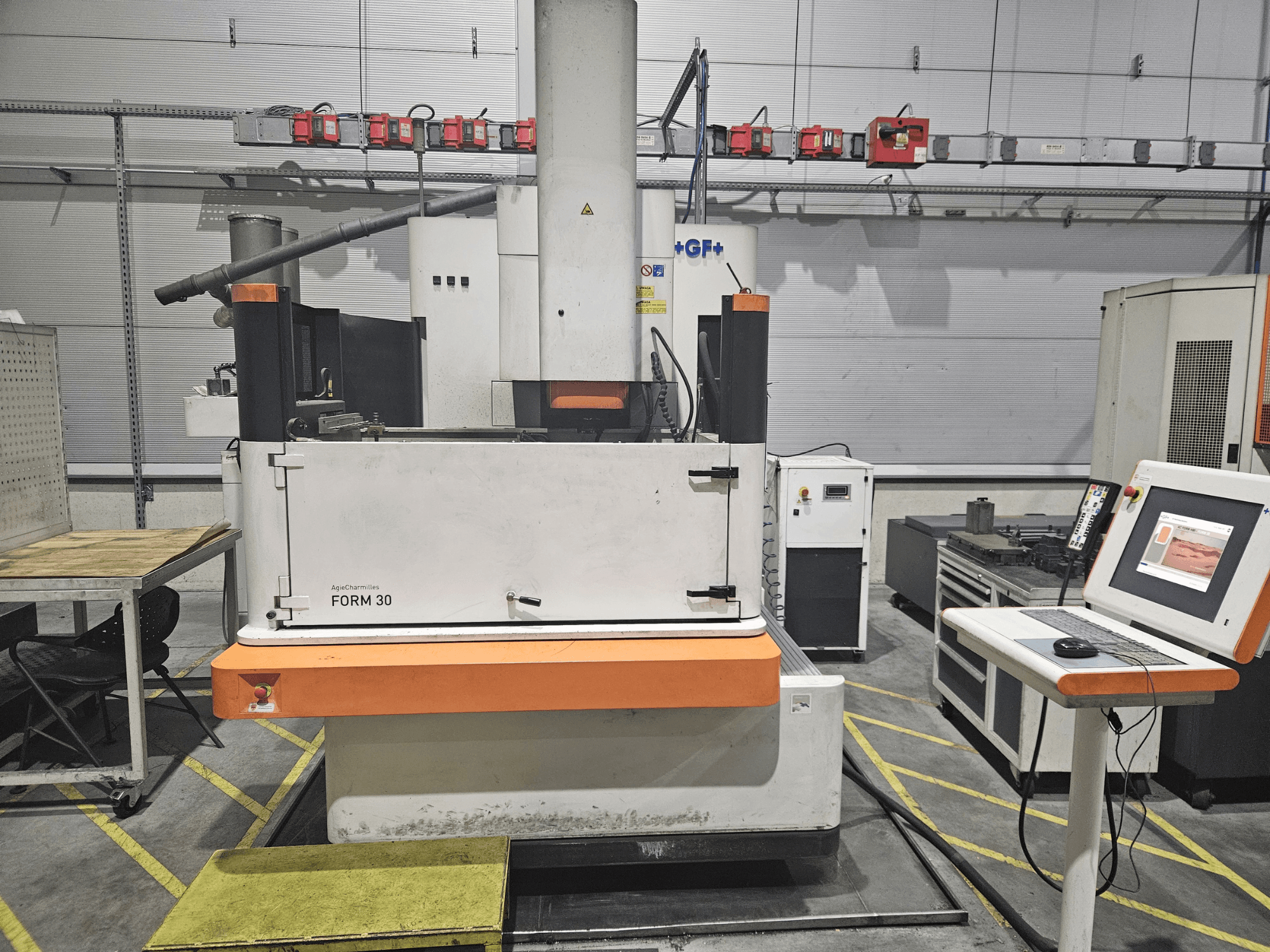 Máquina FORM 30 da ApeqChemicals numa oficina, vista frontal com painel de controlo e mesa de trabalho ao lado.