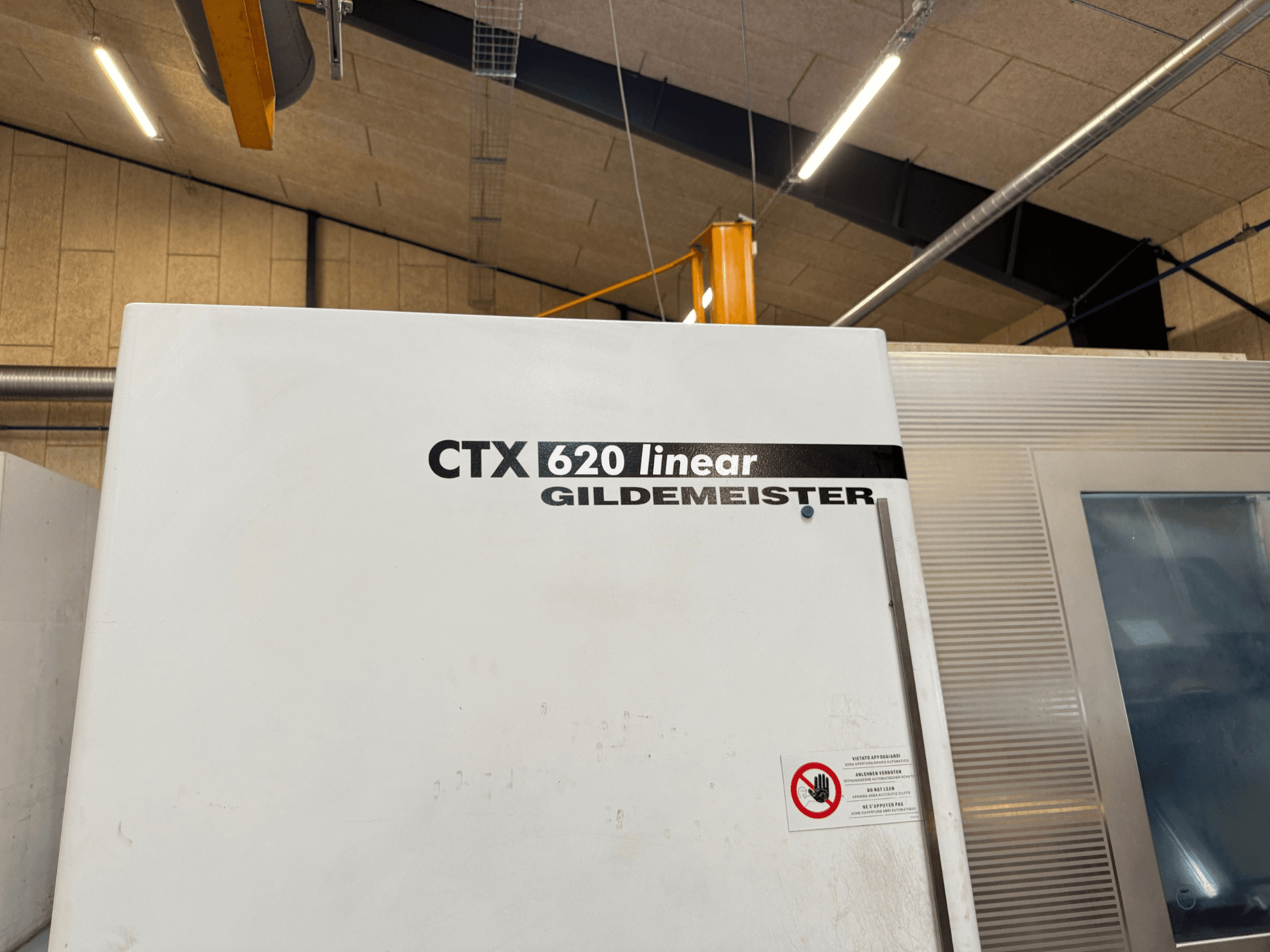 Vista lateral da máquina CTX 620 Linear Gildemeister, com um exterior branco e etiquetas de aviso de segurança.