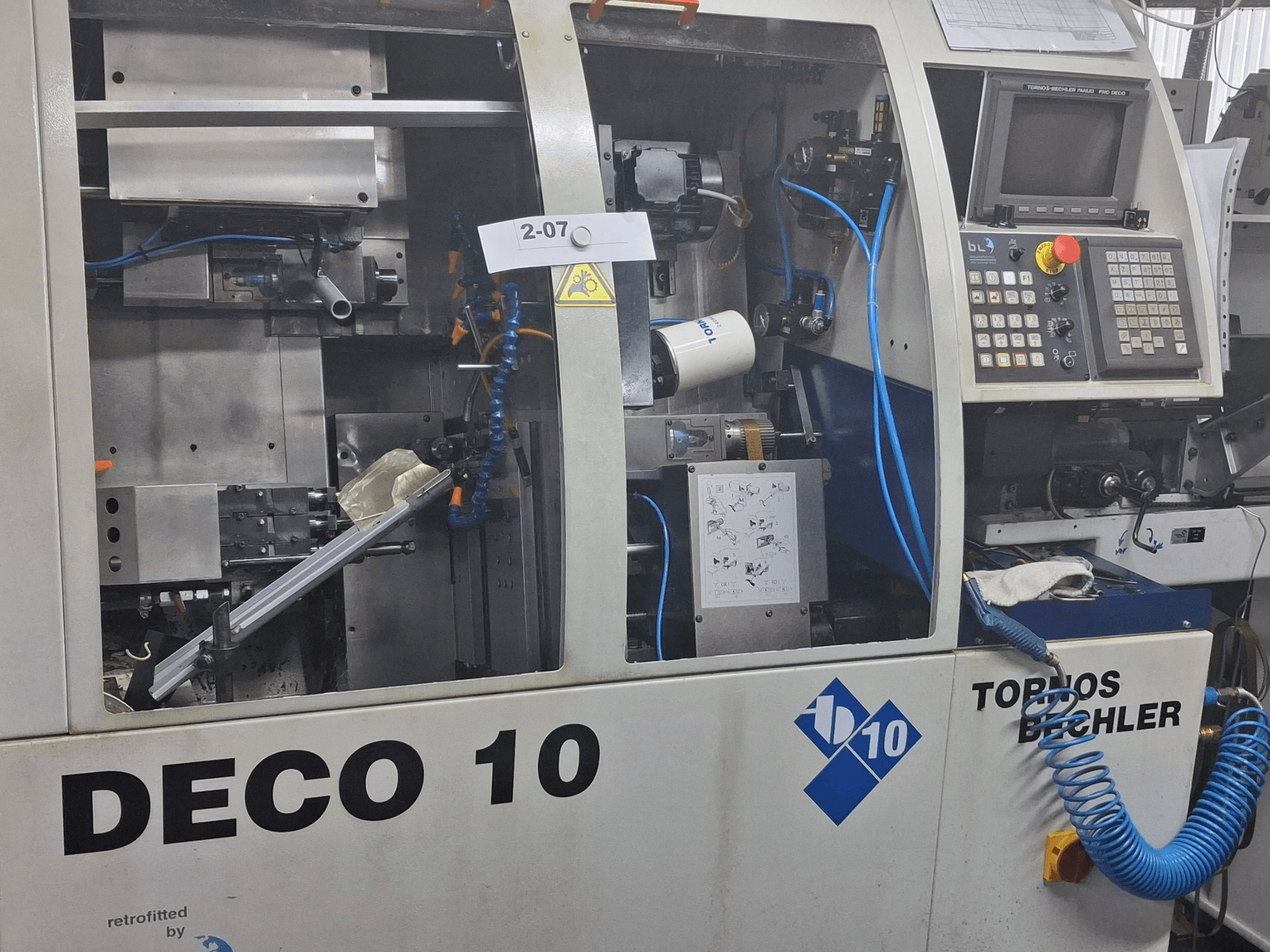 Vista em grande plano do torno TORNOS Deco 10a de tipo suíço, mostrando o mecanismo interno e os detalhes do painel de controlo.