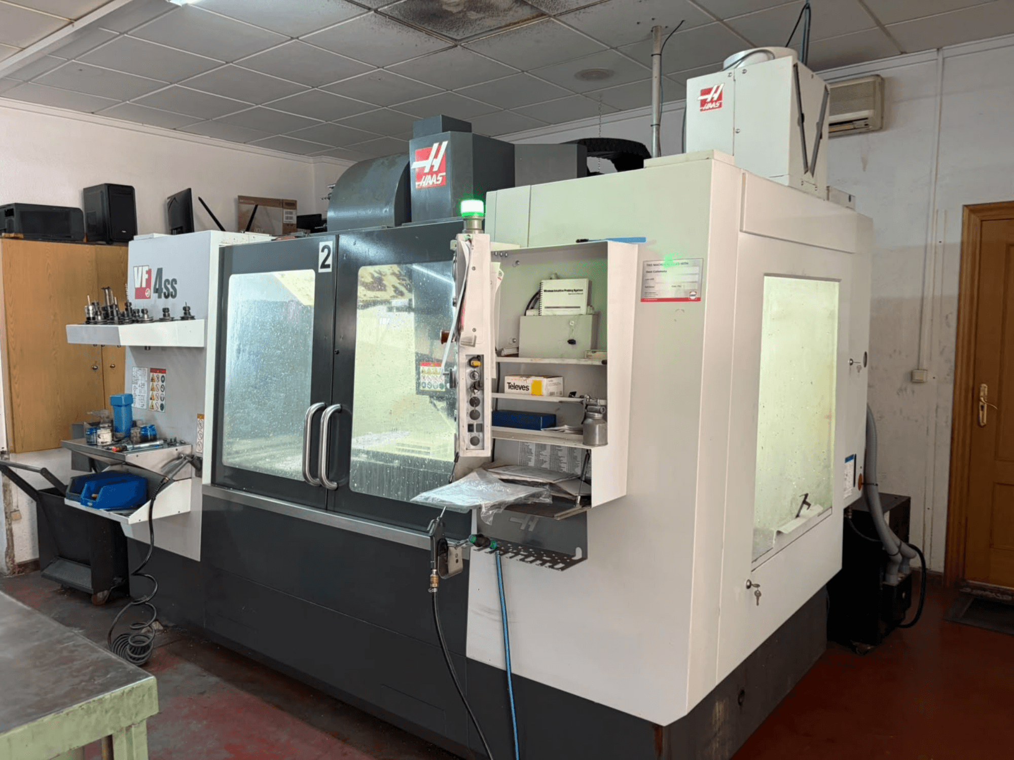 Centro de maquinagem vertical HAAS VF 4SS numa oficina, vista frontal, mostrando o painel de controlo e a área de trabalho com ferramentas e materiais.