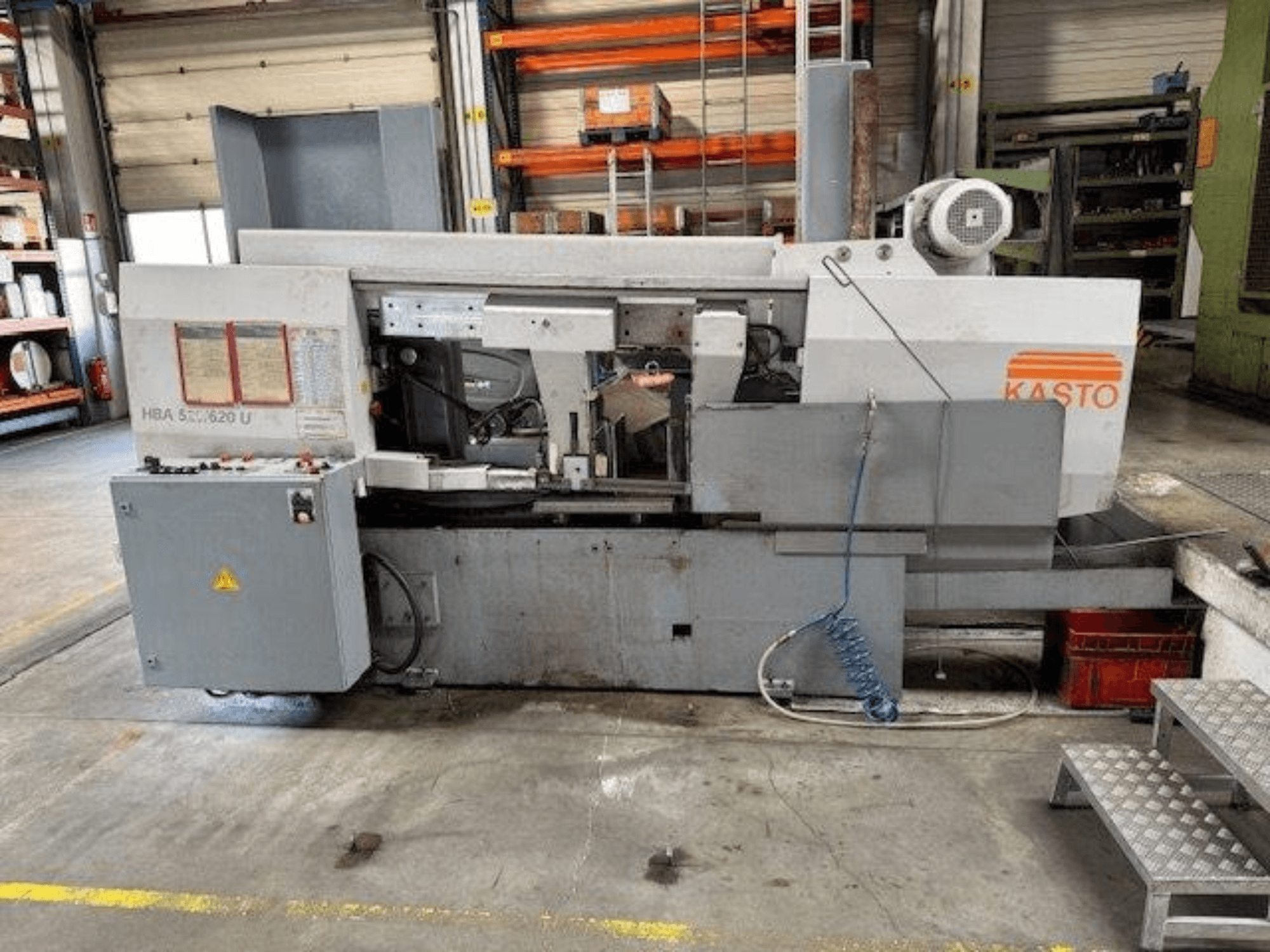 Serra de fita para metal KASTO HBA 520/620 U, vista lateral, mostrando o painel de controlo e a área de corte numa oficina.