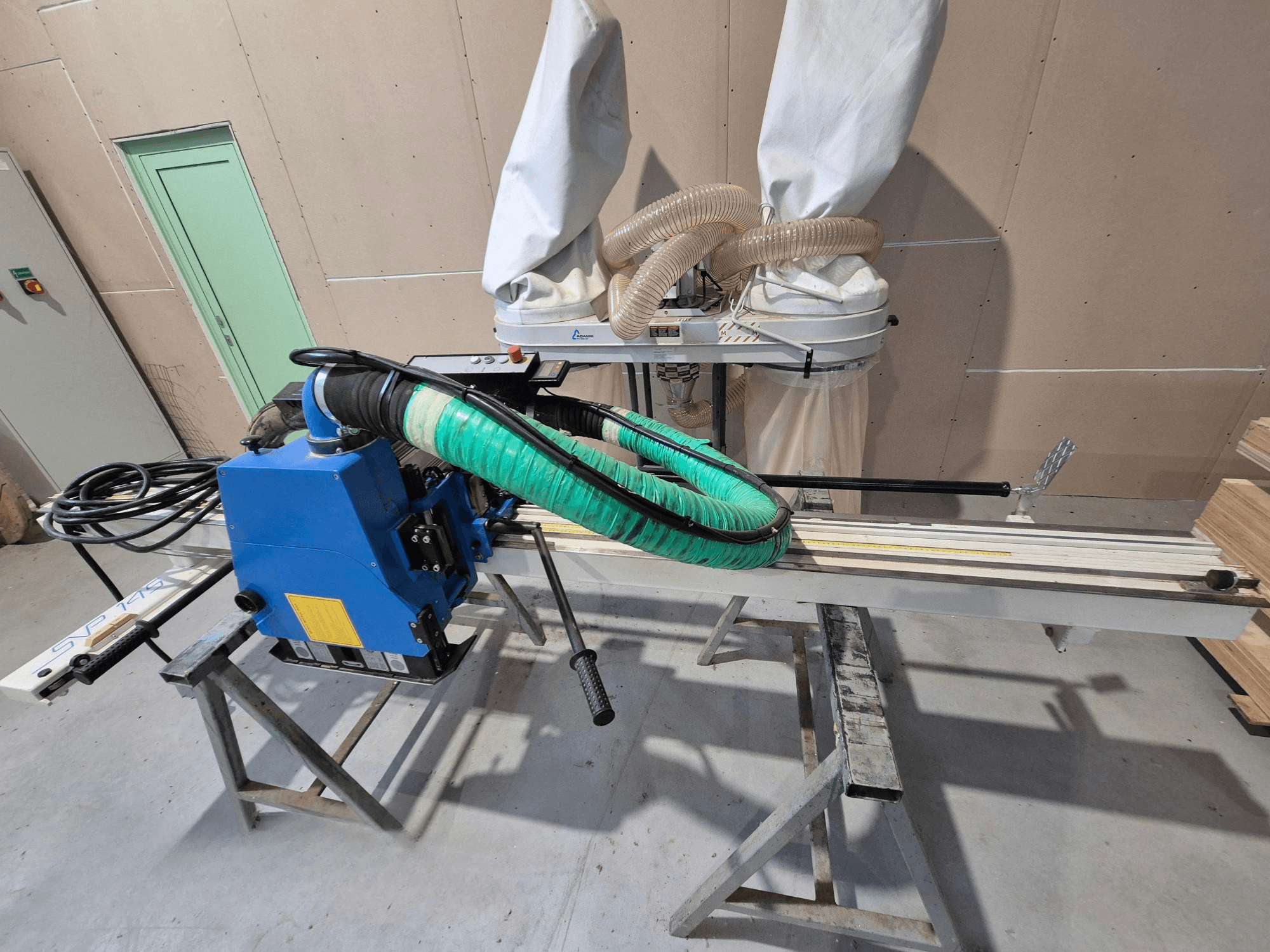 Serra de painel horizontal SVP-175 azul com mangueira de pó verde e suporte, vista de lado numa oficina.