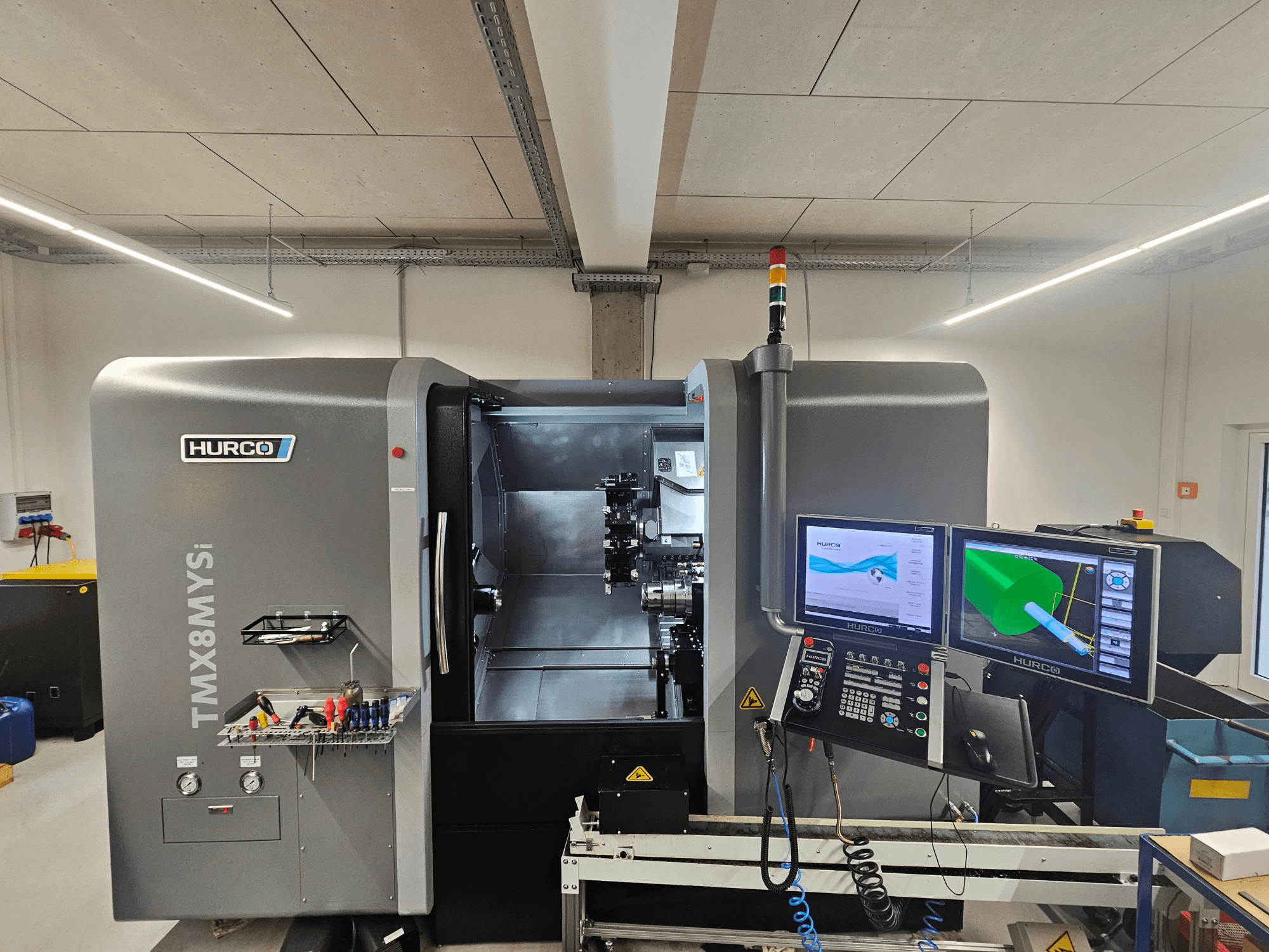Centro de torneamento-fresagem Hurco TMX 8 MYSi numa oficina, com dois monitores, painel de controlo e ferramentas na lateral.