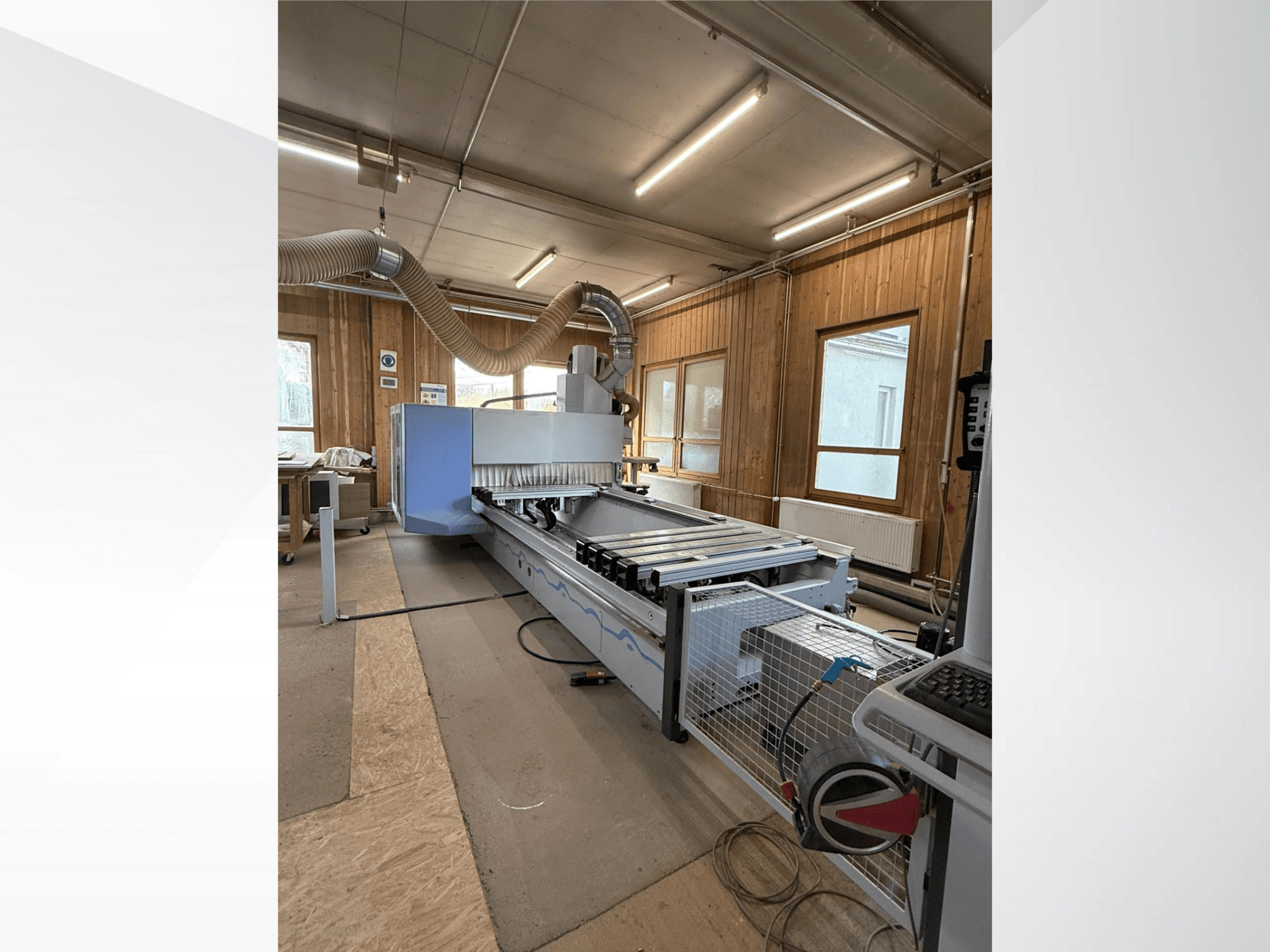 Fresadora CNC numa oficina, vista lateral, com um grande corpo azul, correia transportadora anexa e painel de controlo visível.