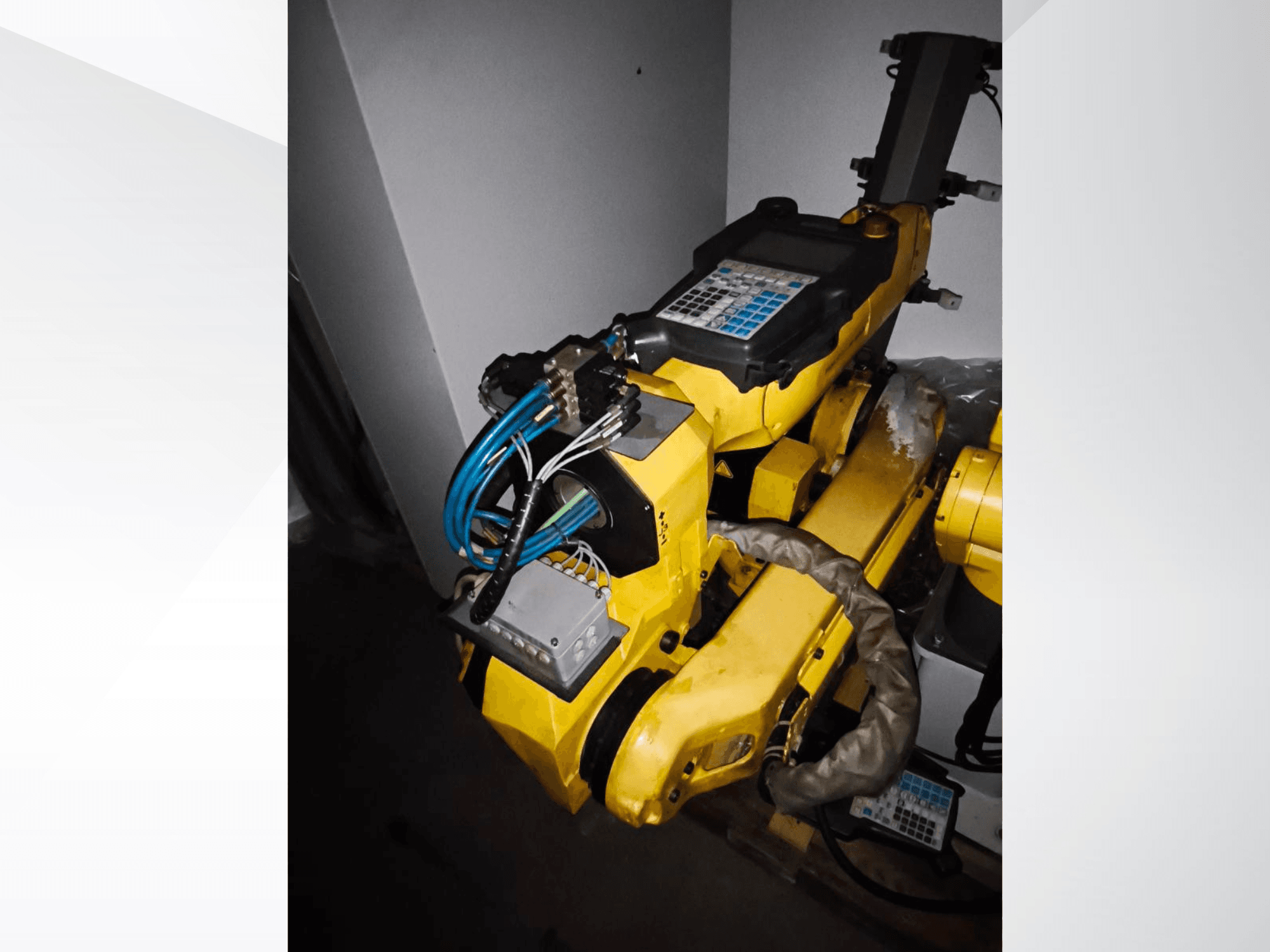 Braço do robô FANUC M-20iA numa vista lateral, mostrando o corpo amarelo, o painel de controlo e a cablagem ligada.