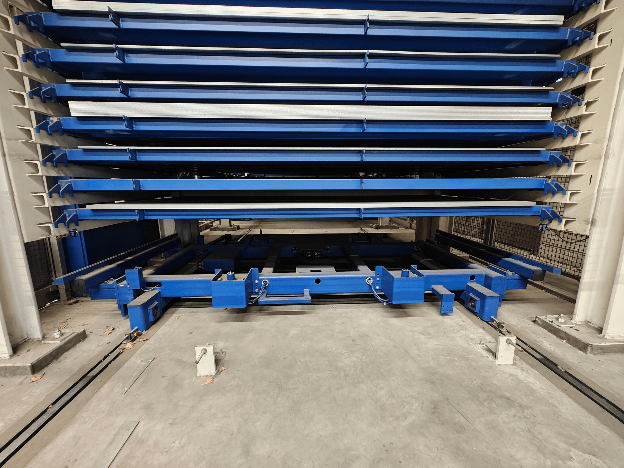 Estante de armazenamento industrial azul com várias prateleiras horizontais, vista de frente. Com mecanismo de elevação e vigas de suporte.
