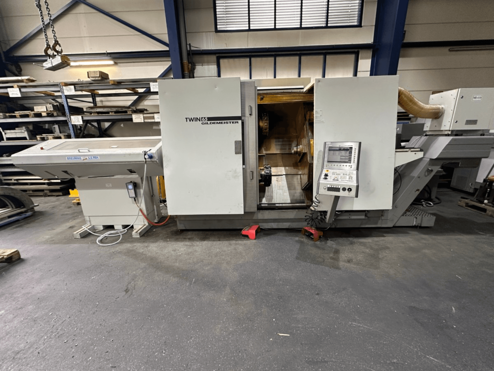 Torneiro horizontal Gildemeister TWIN 65, vista frontal; possui painel de controlo e interior visível para maquinação de peças.