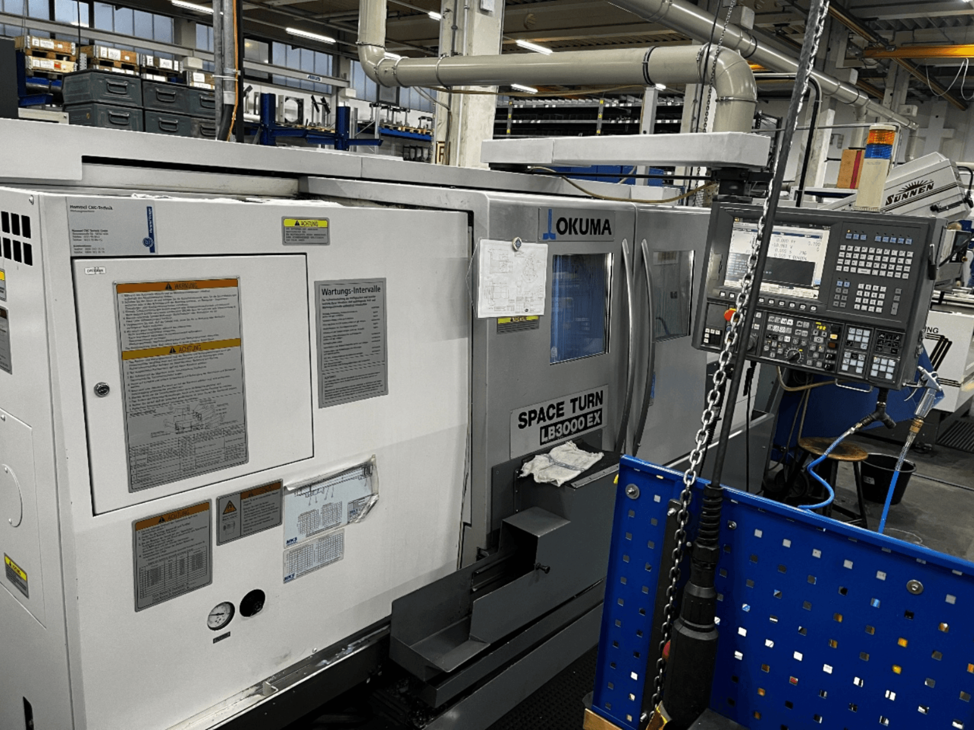 Torneiro horizontal Okuma LB3000 EX, vista frontal, com painel de controlo e informações de segurança na lateral.