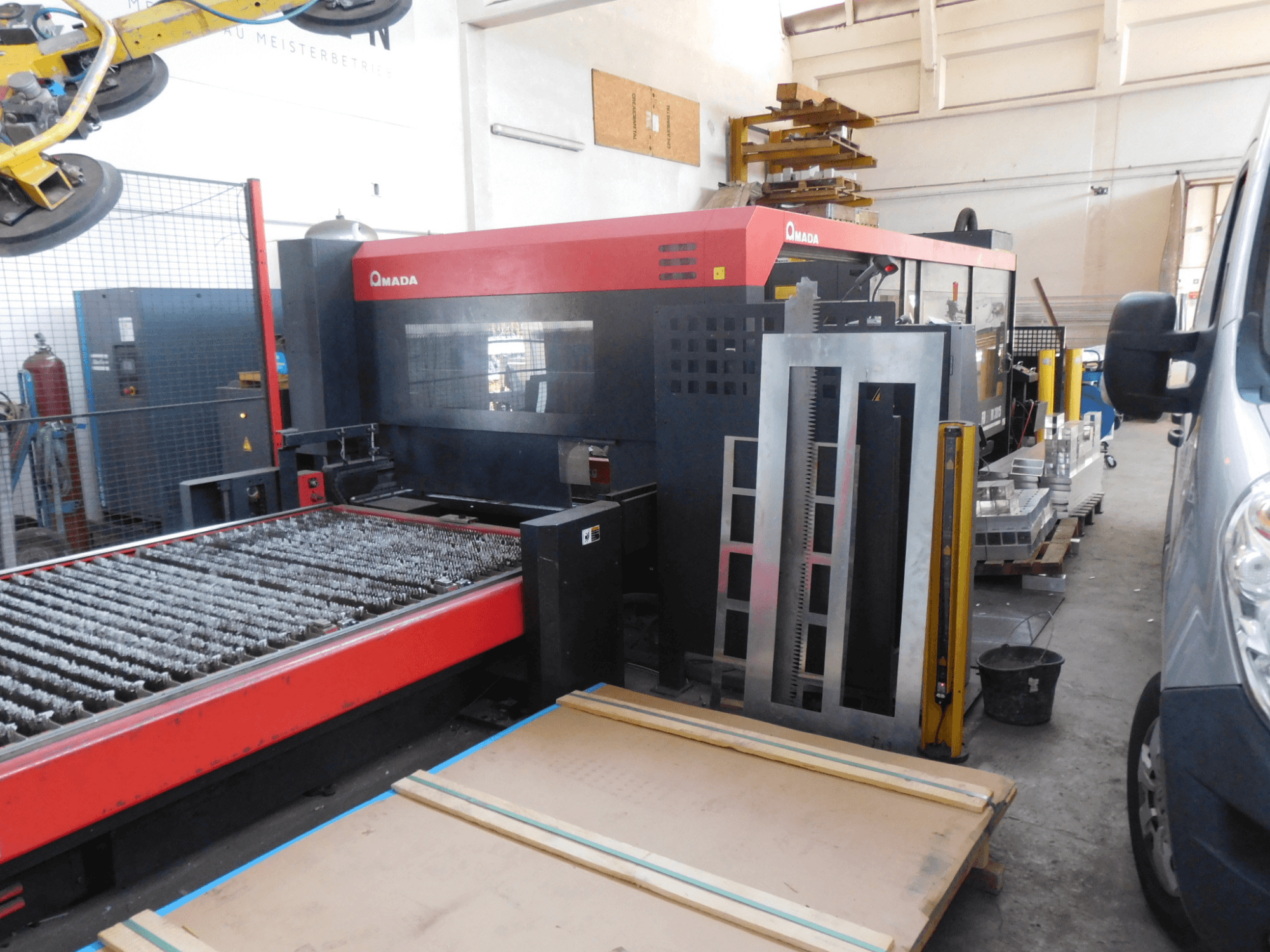 Vista frontal da máquina de corte a laser AMADA FO-3015 II RI CO2, com uma base de corte e área de trabalho circundante.