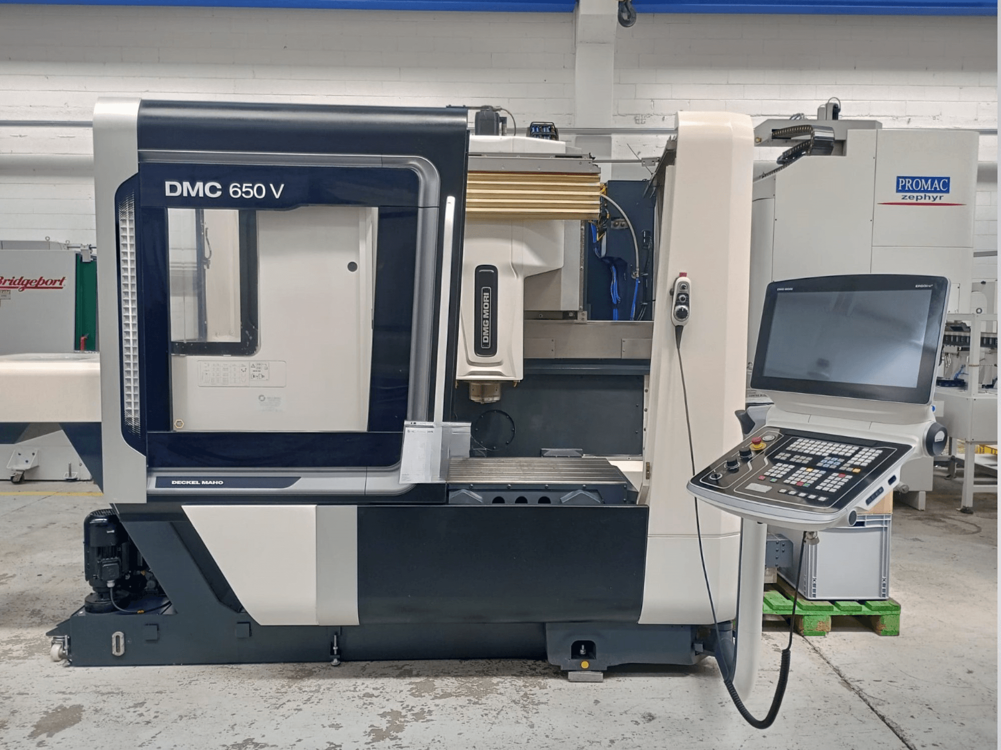 Vista lateral de uma máquina CNC Decker Maho DMC 650 V, com um painel de controlo com botões e um ecrã, em ambiente industrial.