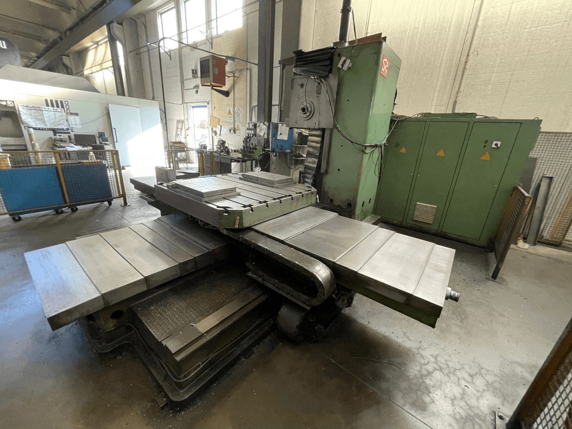 Fresadora industrial de grandes dimensões com um corpo verde, vista lateral, com várias superfícies planas e armários de arrumação em segundo plano.