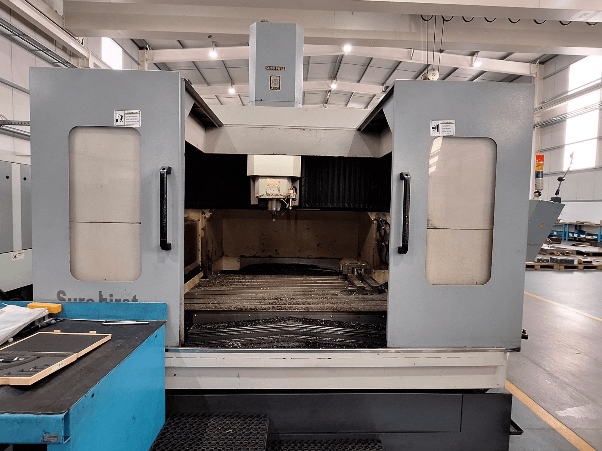 Centro de maquinação vertical Sure First QM-1836, vista frontal mostrando a cabeça da ferramenta e a área de trabalho vazia, ambiente industrial moderno.