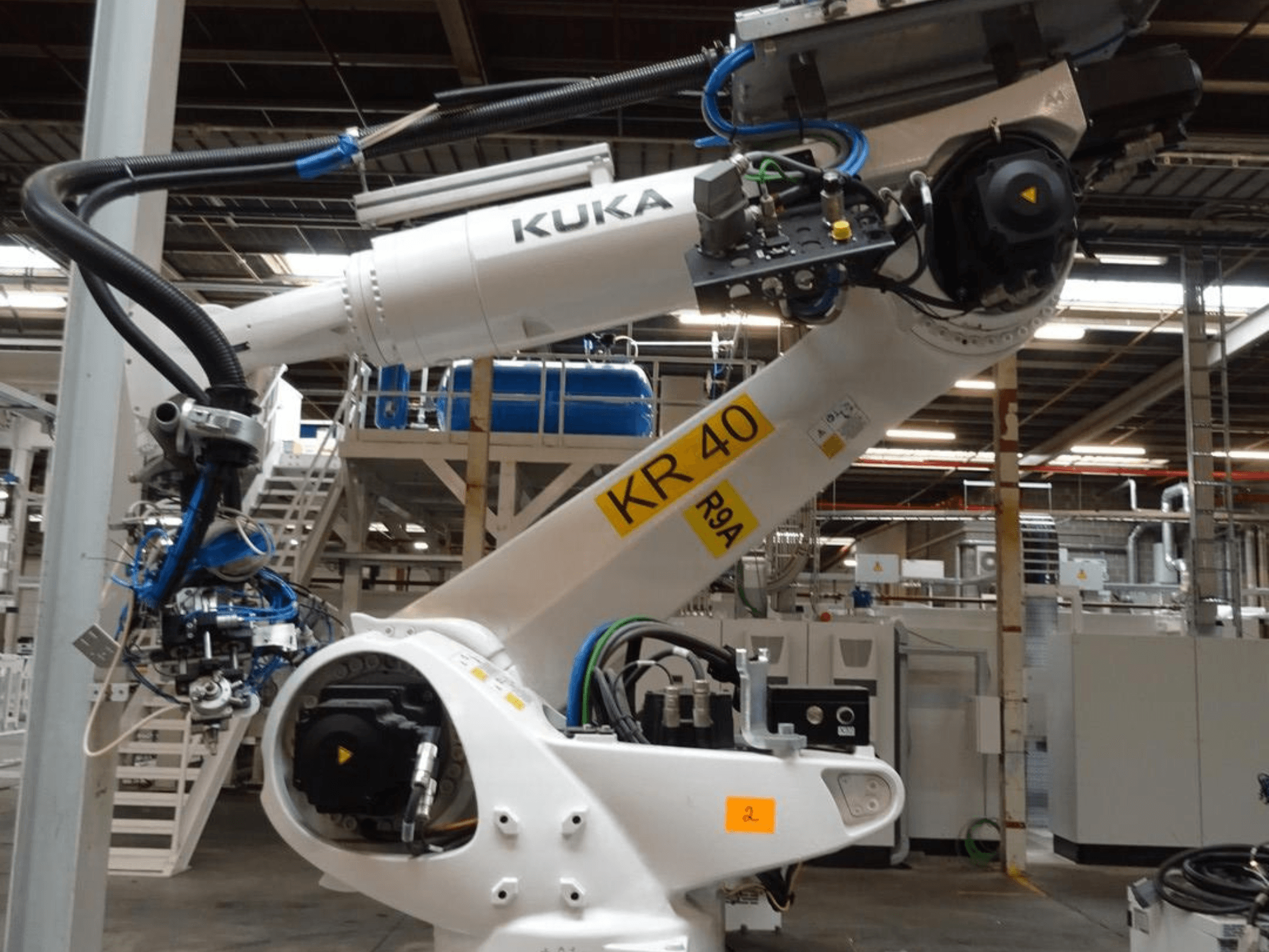 Braço robótico KUKA KR 120 R3100-2 em vista lateral, mostrando o painel de controlo e os componentes mecânicos, num ambiente industrial.