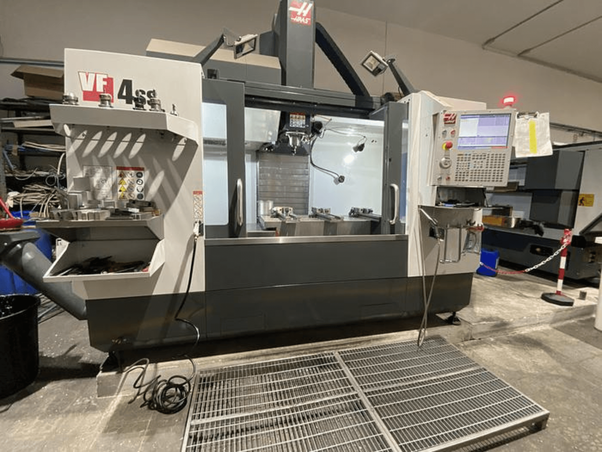 Fresadora CNC Haas VF-4SS, vista frontal, com armazenamento de ferramentas, painel de controlo e área de trabalho visível num ambiente de oficina.