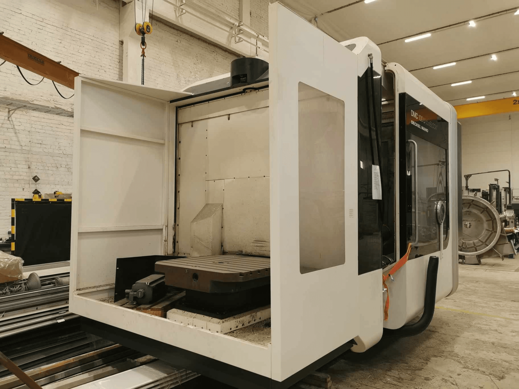 Máquina CNC linear DMC 100U, vista lateral com a porta de acesso aberta, mostrando a mesa de trabalho e os componentes internos.